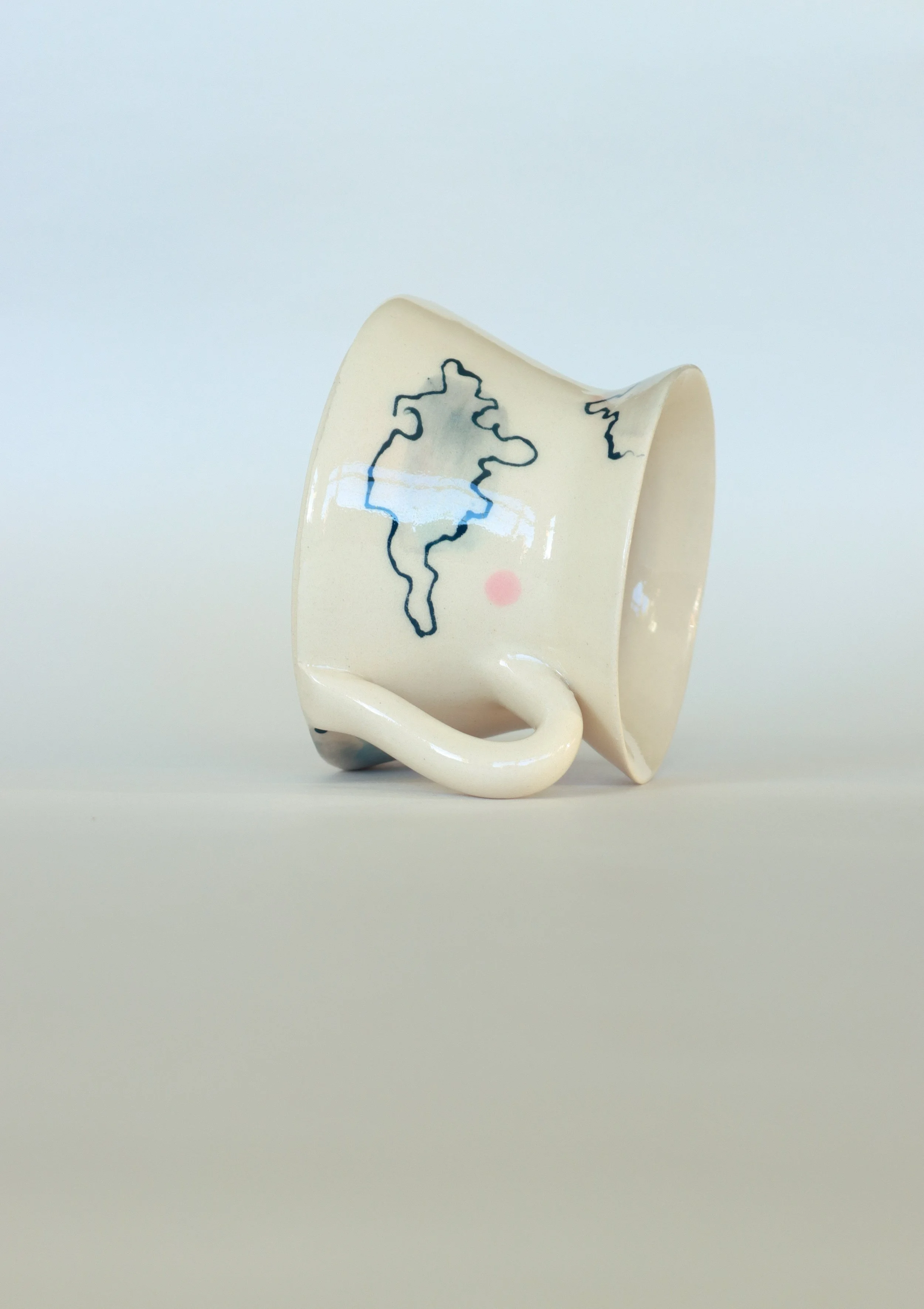 An angular cream cup lies on its side, featuring loose illustrations of clouds on it.
