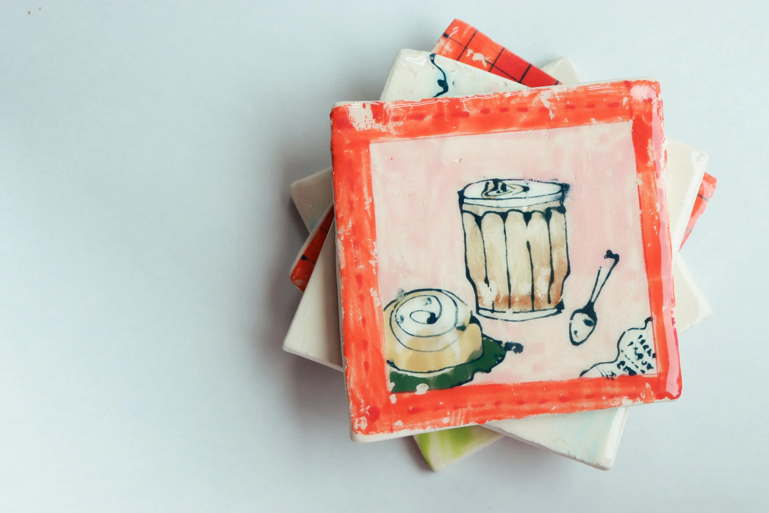 A stack of coasters, the top being a newsprint transfer of a latte, accompanied by a cinnamon bun, spoon, and reciept.