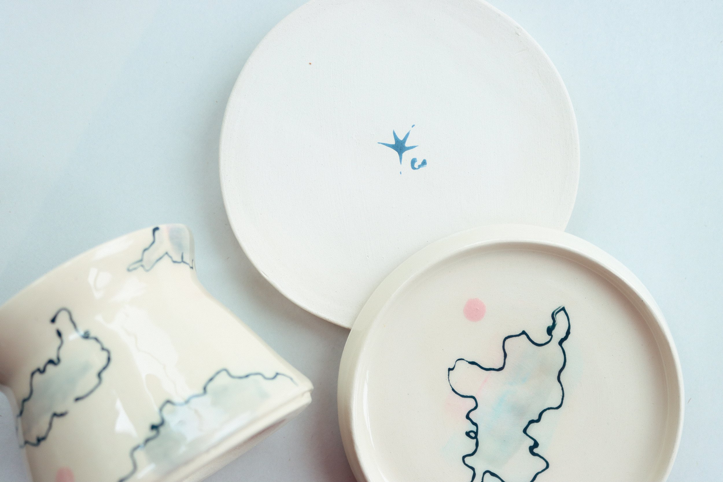 A mug, and two coasters against a white background. All are white, and feature illustrations of clouds.