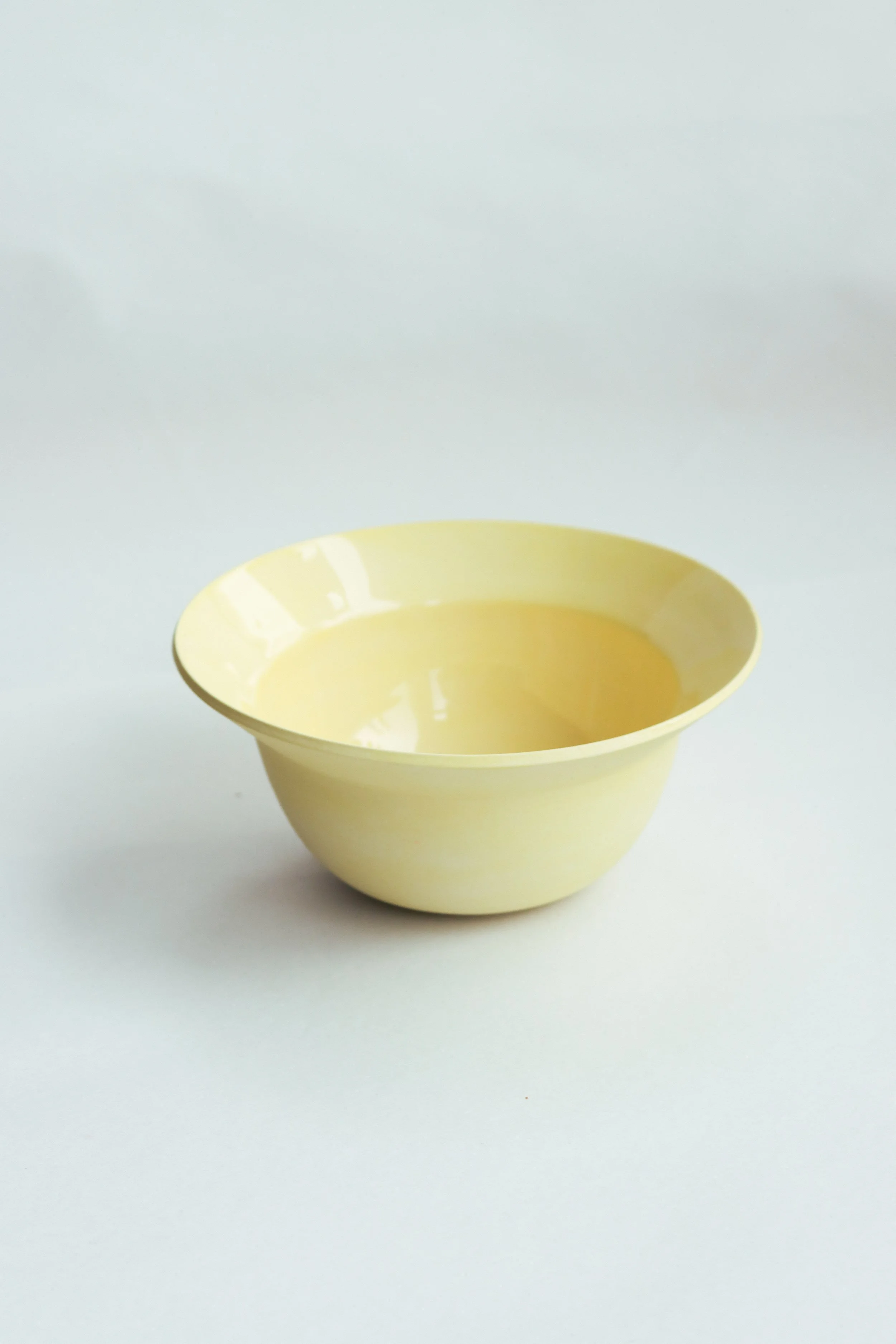 A pale yellow pasta bowl with a wide rim against a white background.