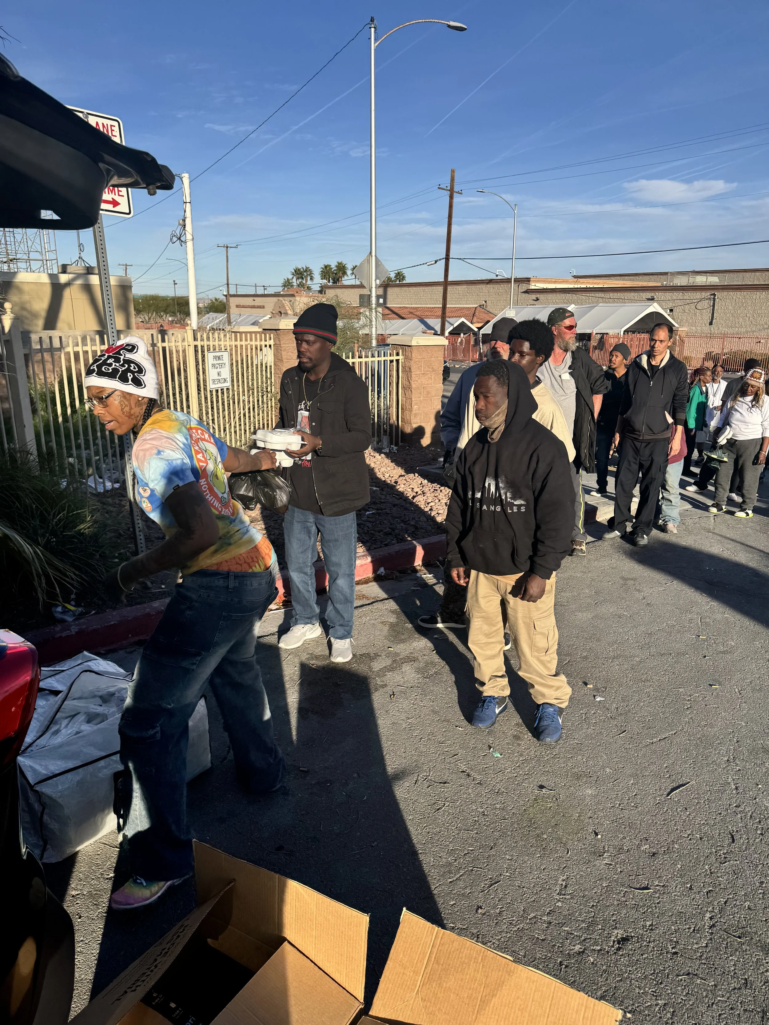 Love Thy Neighbor activation, A group of people standing in line outdoors beside cardboard boxes under a clear blue sky.