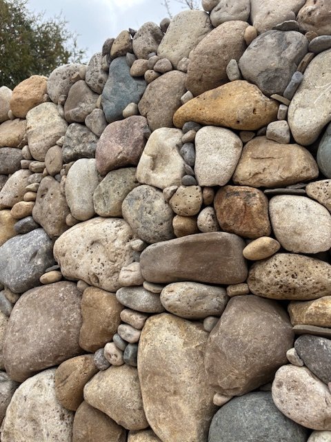 Close-up of a stone wall made of various sizes and colors of rounded and irregular rocks.