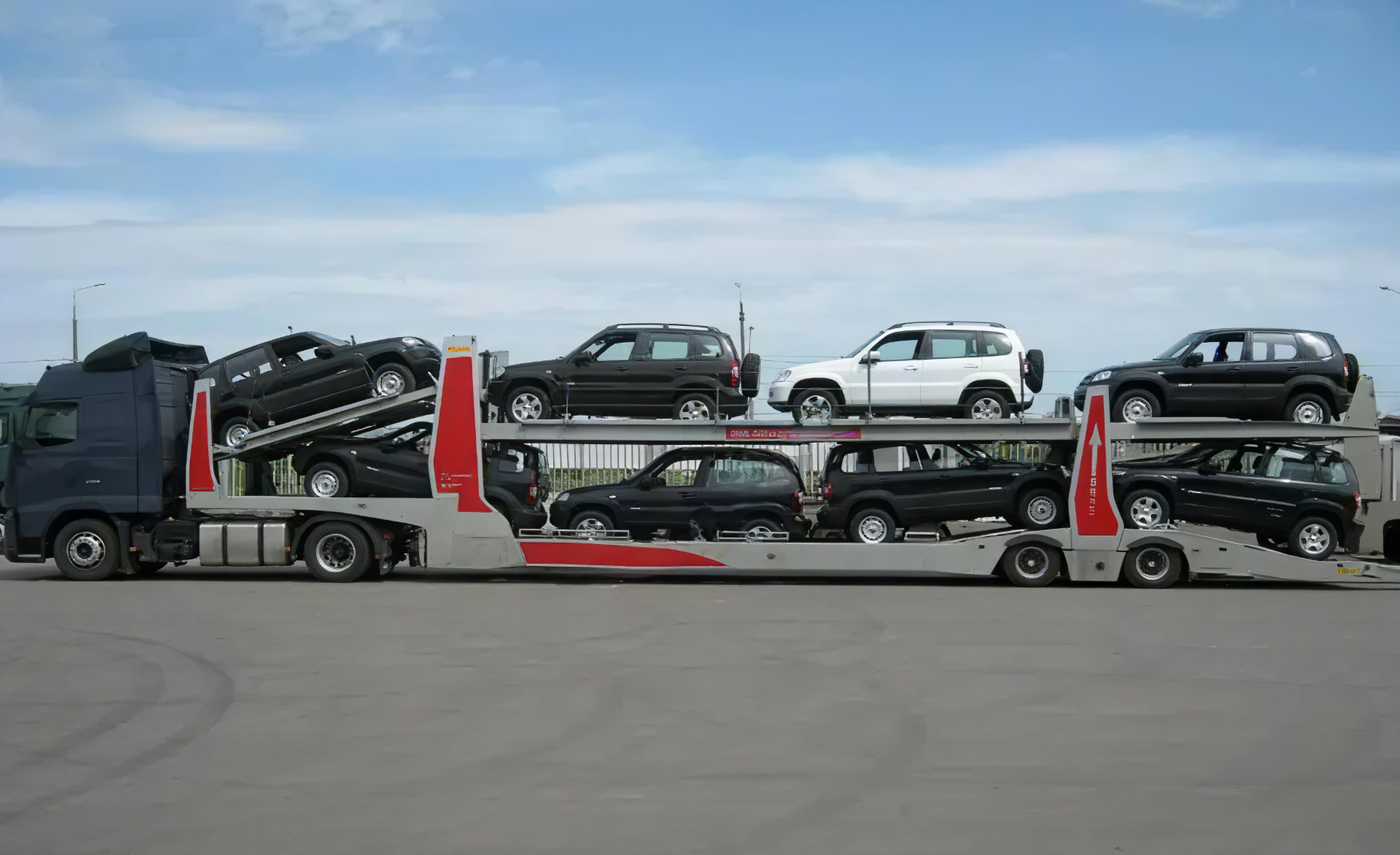 A car carrier truck transporting several black and white cars on two levels under a partly cloudy sky.