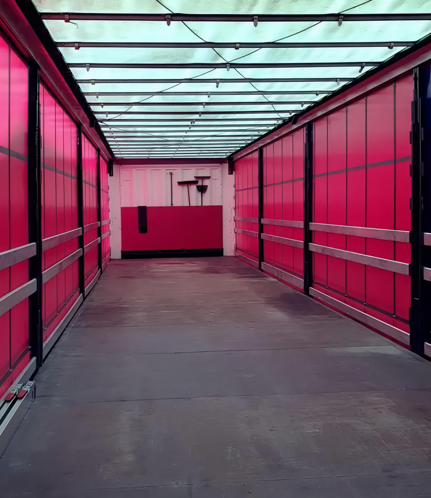 Empty trailer with pink sides, wooden floor, and a transparent roof, with cleaning tools hanging on a white back wall.