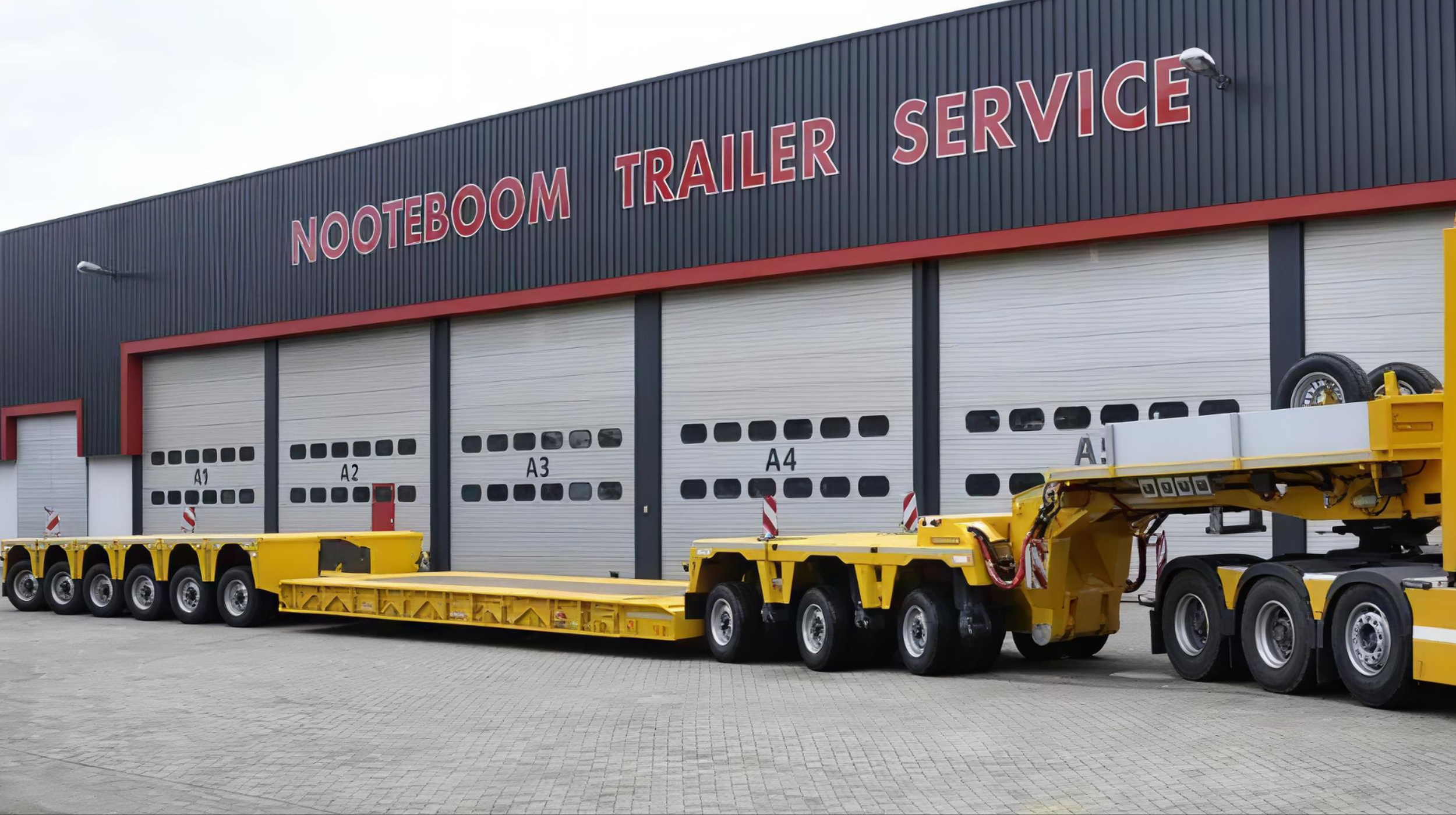 Large building with a sign that reads 'Nooteboom Trailer Service,' with multiple trailer doors and yellow trailer transport vehicles parked in front.