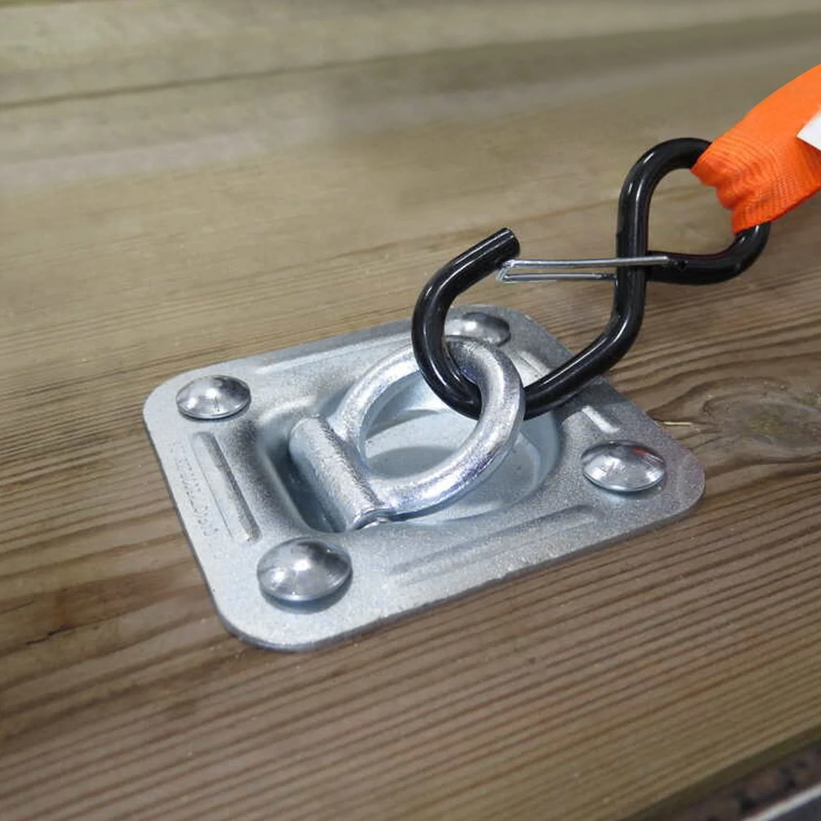 Close-up of a heavy-duty eye bolt with a carabiner attached, mounted on a metal plate on a wooden surface.