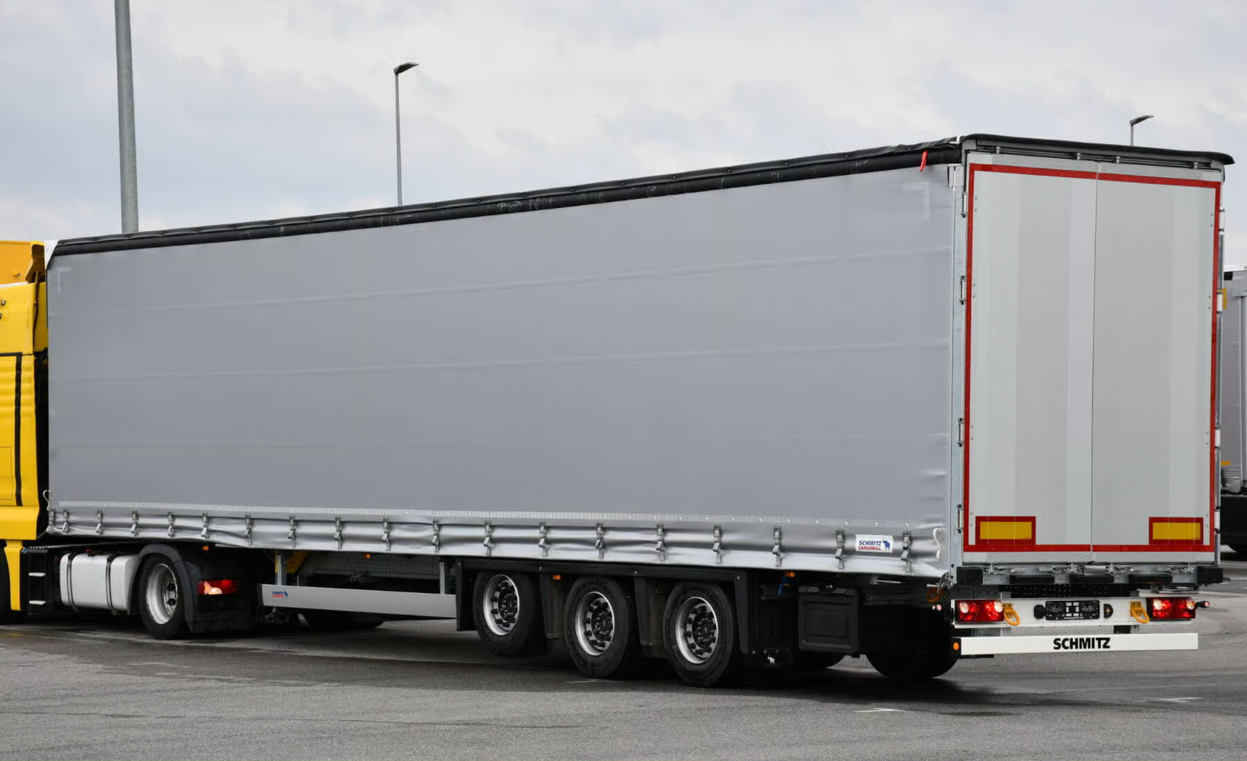 A large gray trailer attached to a truck parked on a paved lot with streetlights visible in the background.