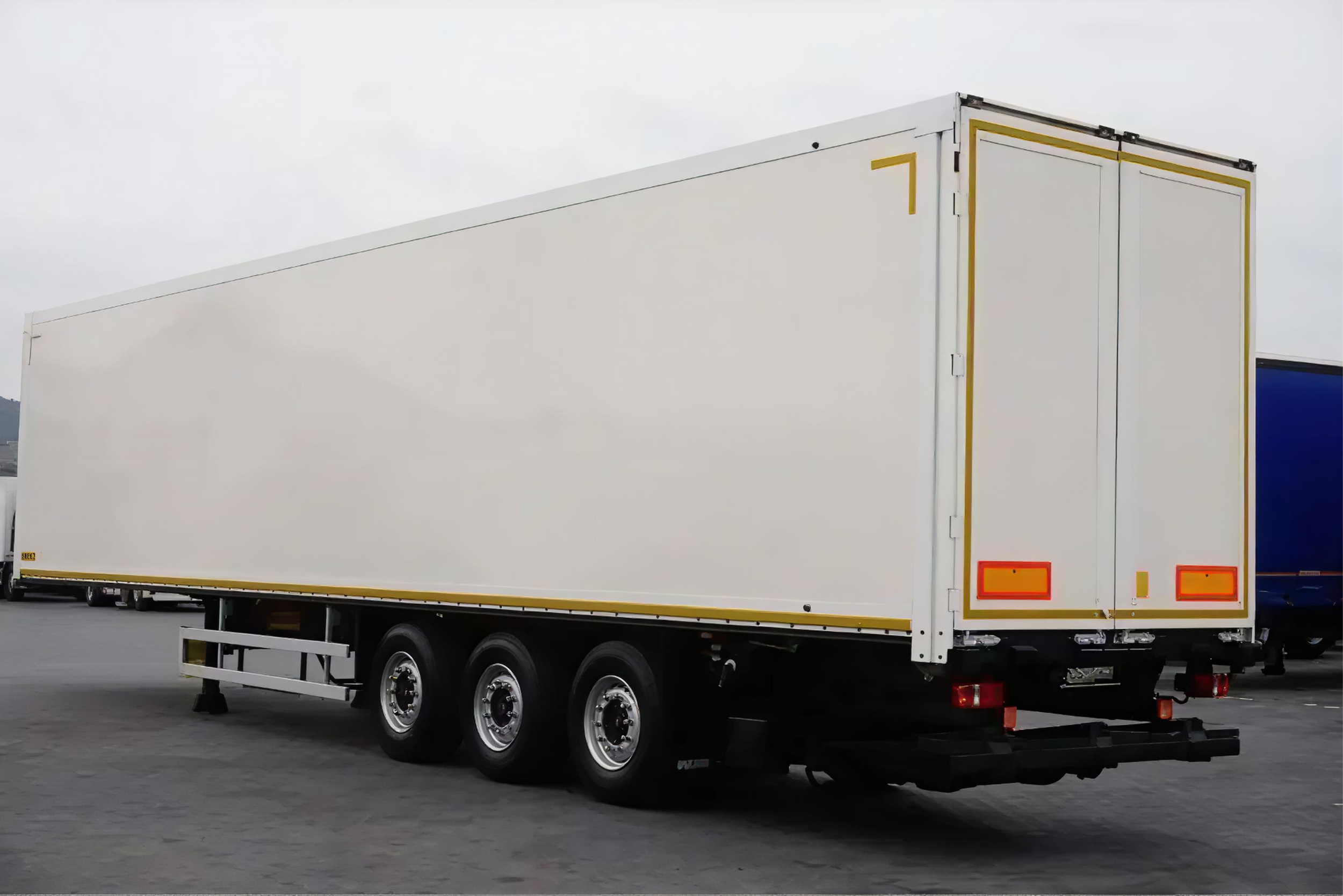 A white semi-truck trailer parked on asphalt, with a small white barrier in front, and gray sky in the background.