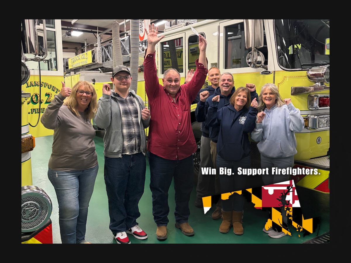 Group of people celebrating in front of a fire truck, some raising their fists and smiling.