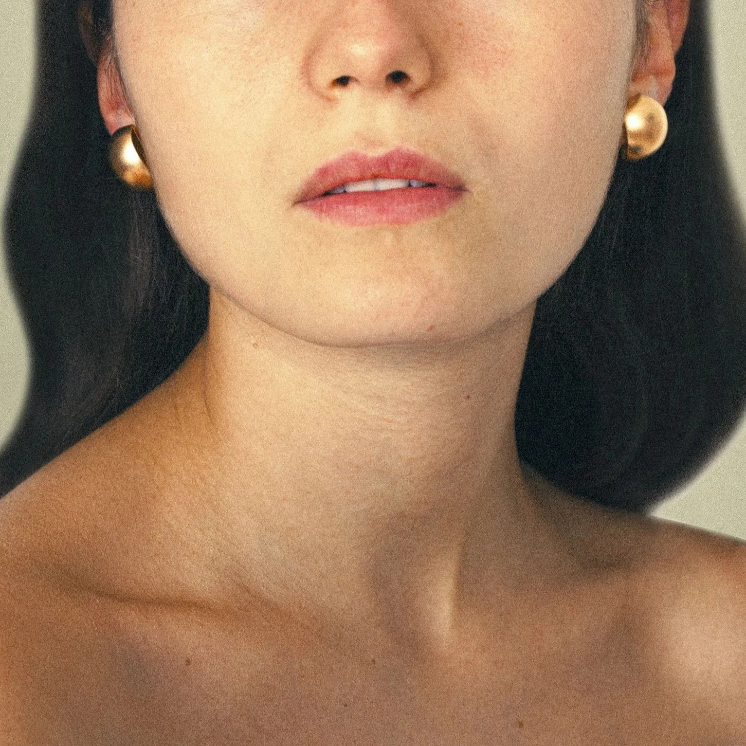 Nahaufnahme eines Frauenhalses und Kiefers mit goldenen Ohrringen.