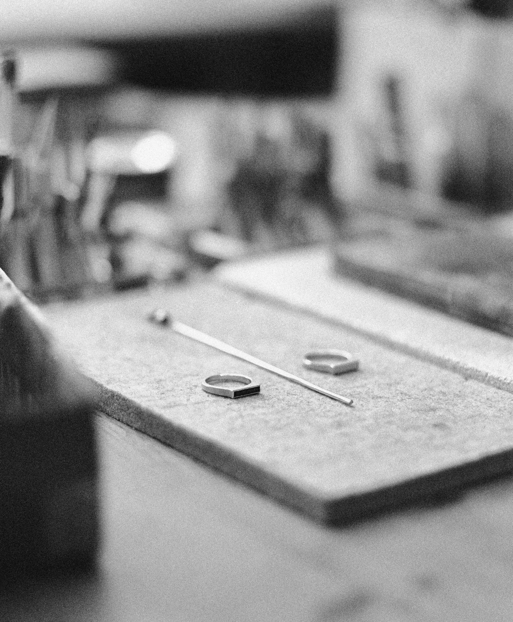 Schwarz-Weiß-Bild einer Werkbank mit zwei Metallringen und einem dünnen Silber Stück darauf.