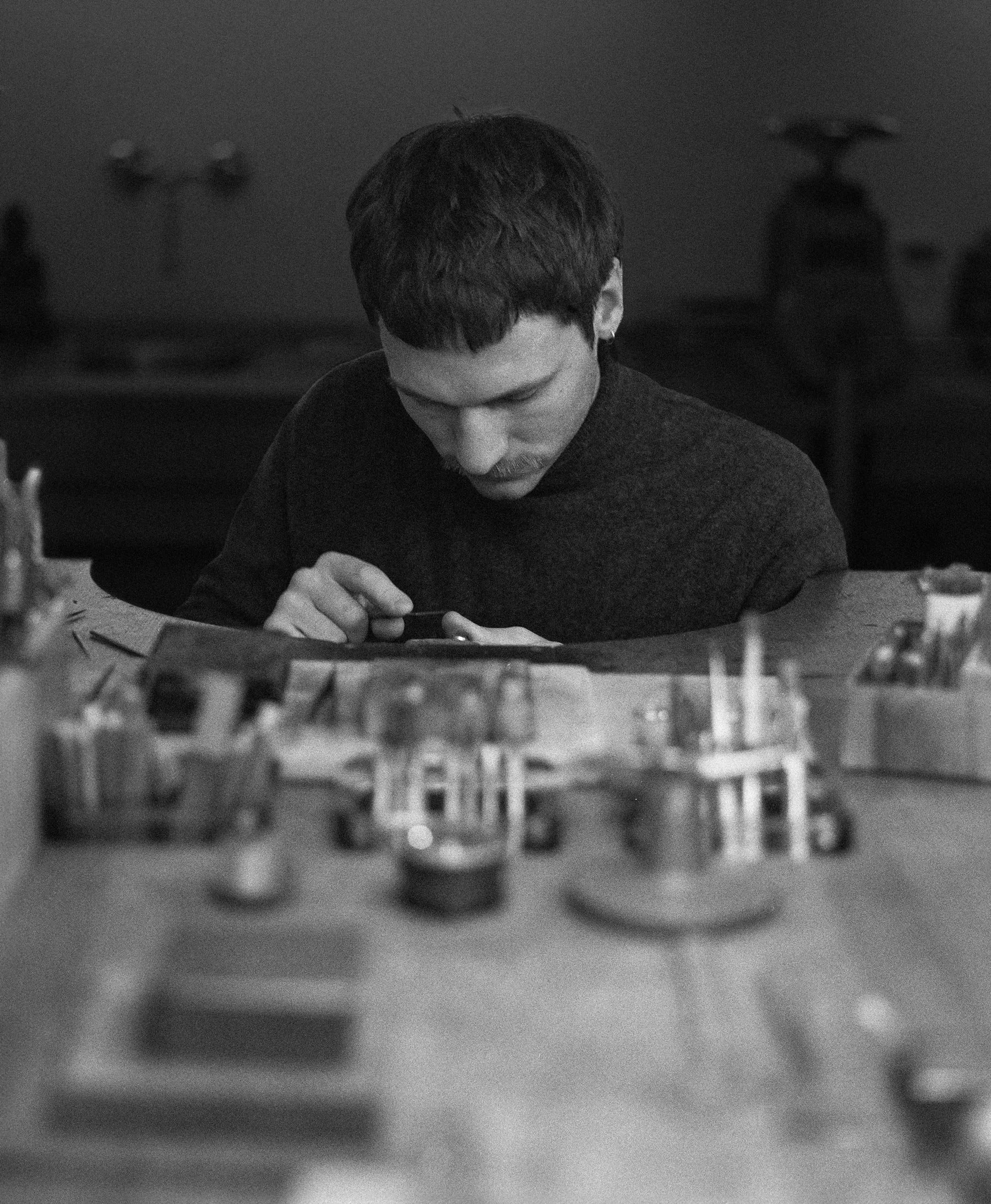 Xaver Vogl sitzt an einem Tisch, betrachtet ein kleine Schmuckstück, umgeben von Werkzeug, in seiner Werkstatt in der Klenzestraße 23.