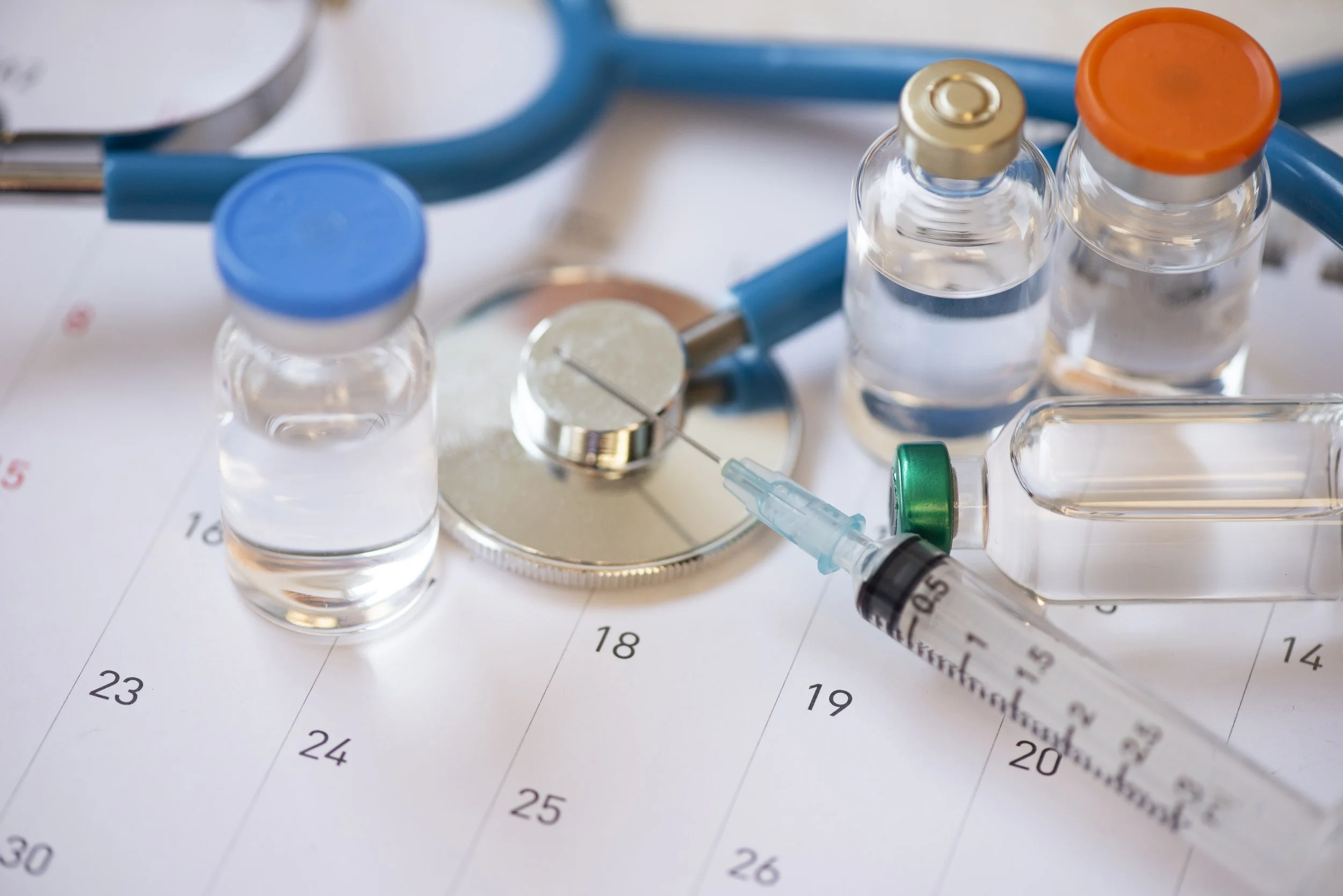 Medical vials, a syringe, and a stethoscope placed on a calendar.