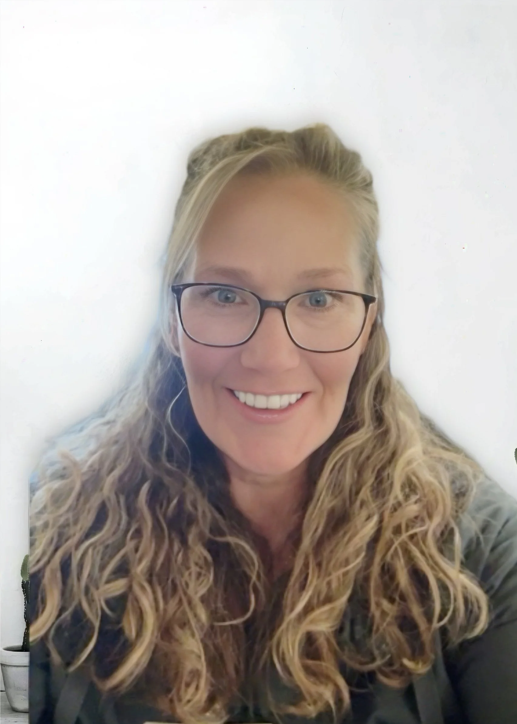 A smiling woman with curly blonde hair, glasses, and blue eyes, wearing a dark jacket, against a plain white background.