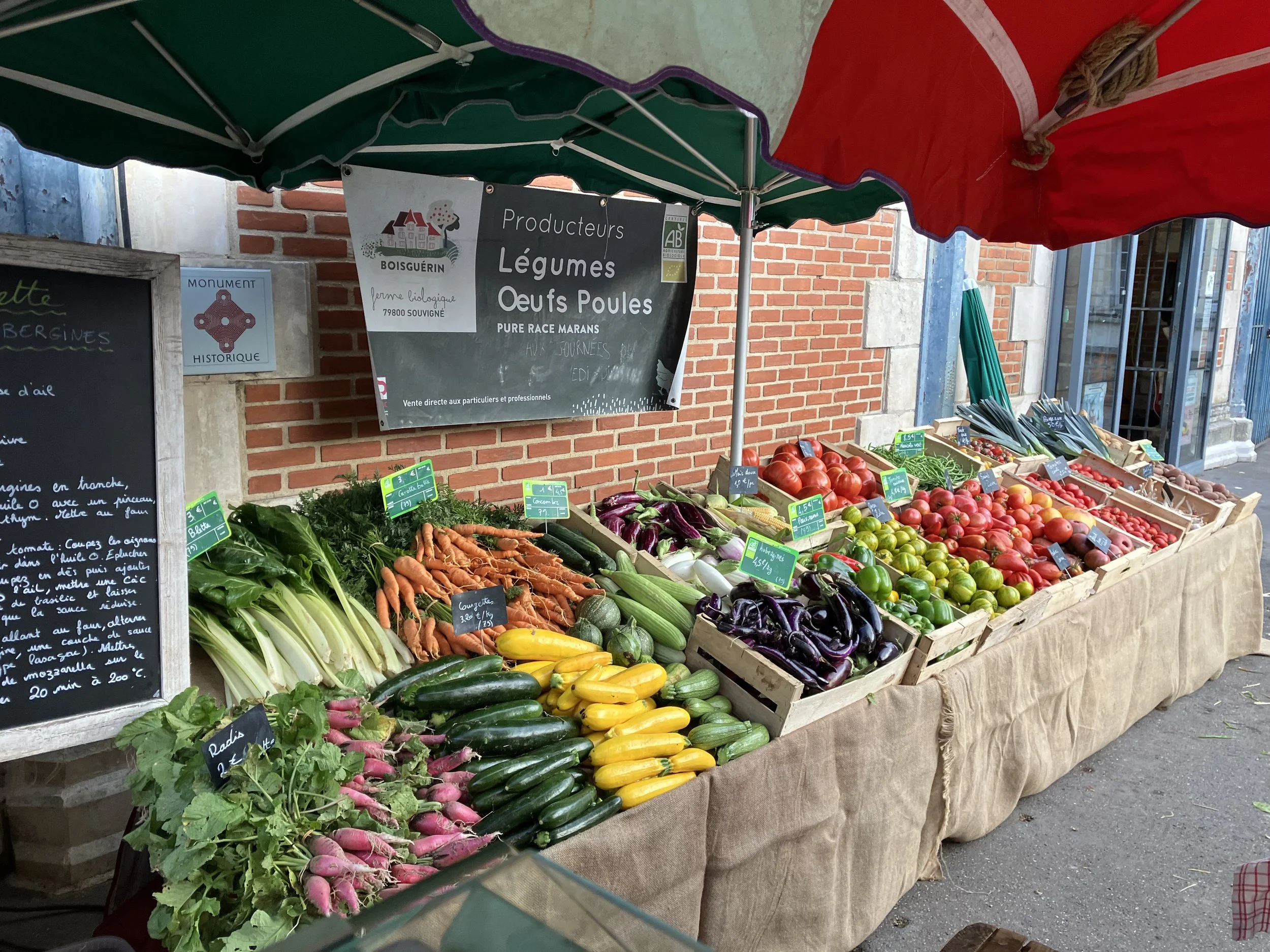 Vente de légumes, œufs, poules au marché avec une bannière indiquant 'Producteurs Légumes Œufs Poules'.