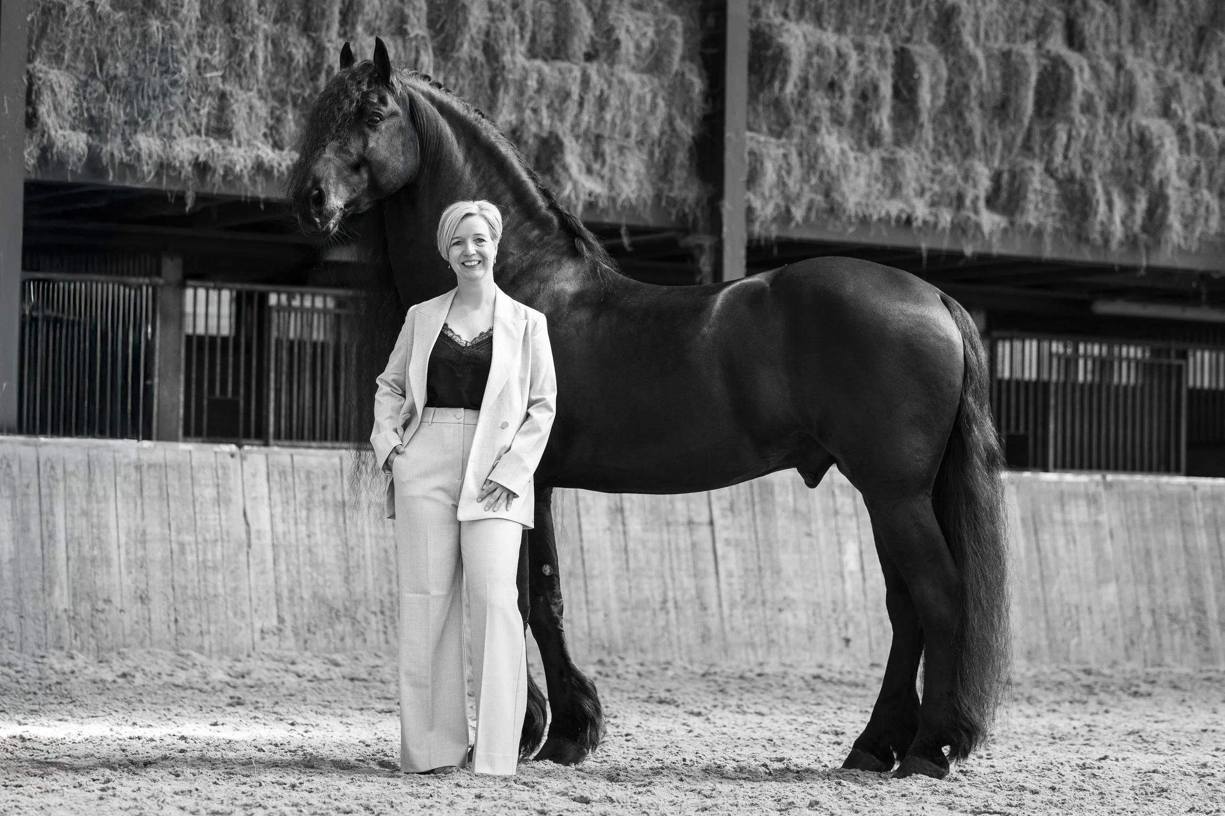 Rianne Sibma naast haar Friese paard William in de rijhal, in zwart-wit