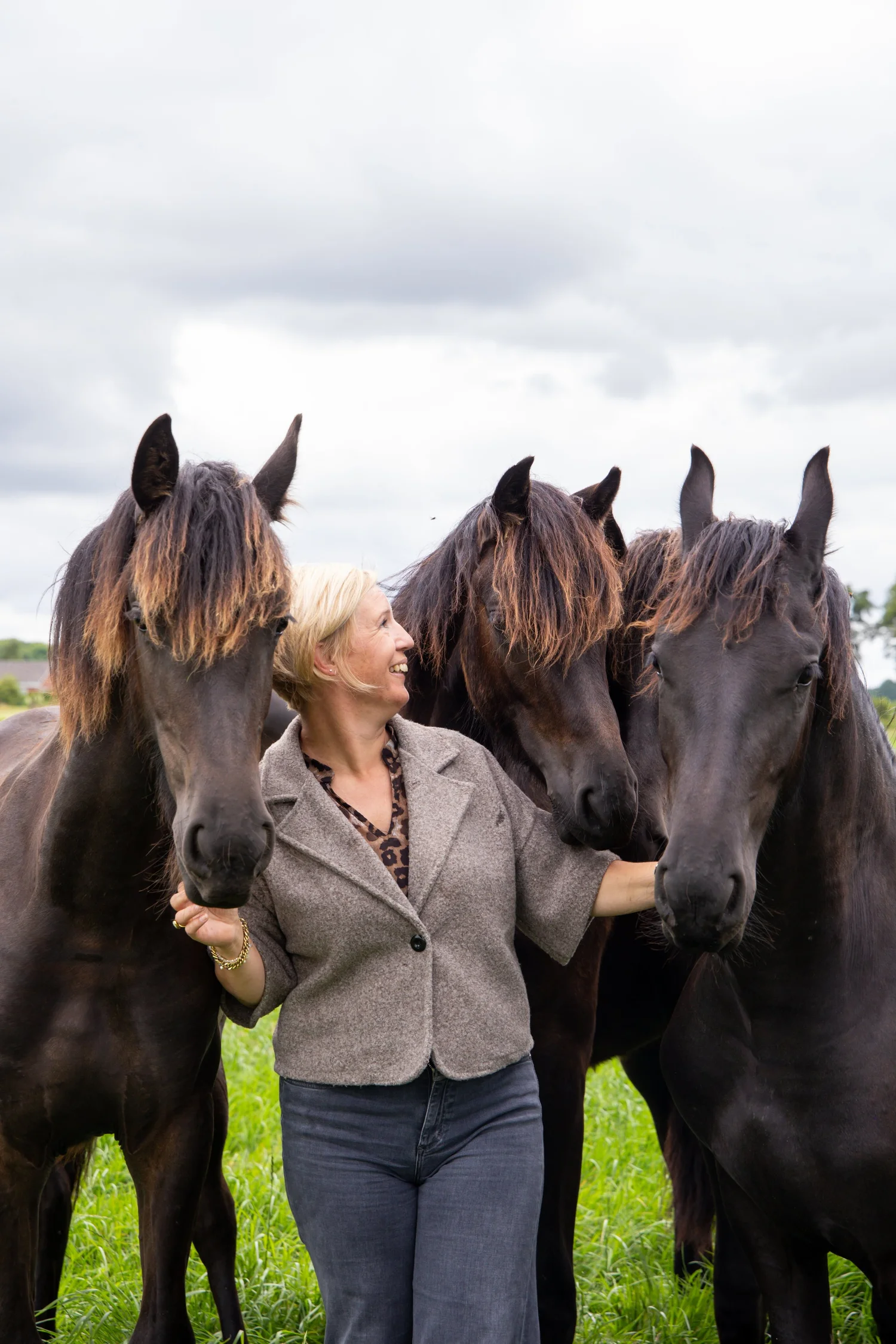 Rianne Sibma lachend tussen drie losse Friese paarden