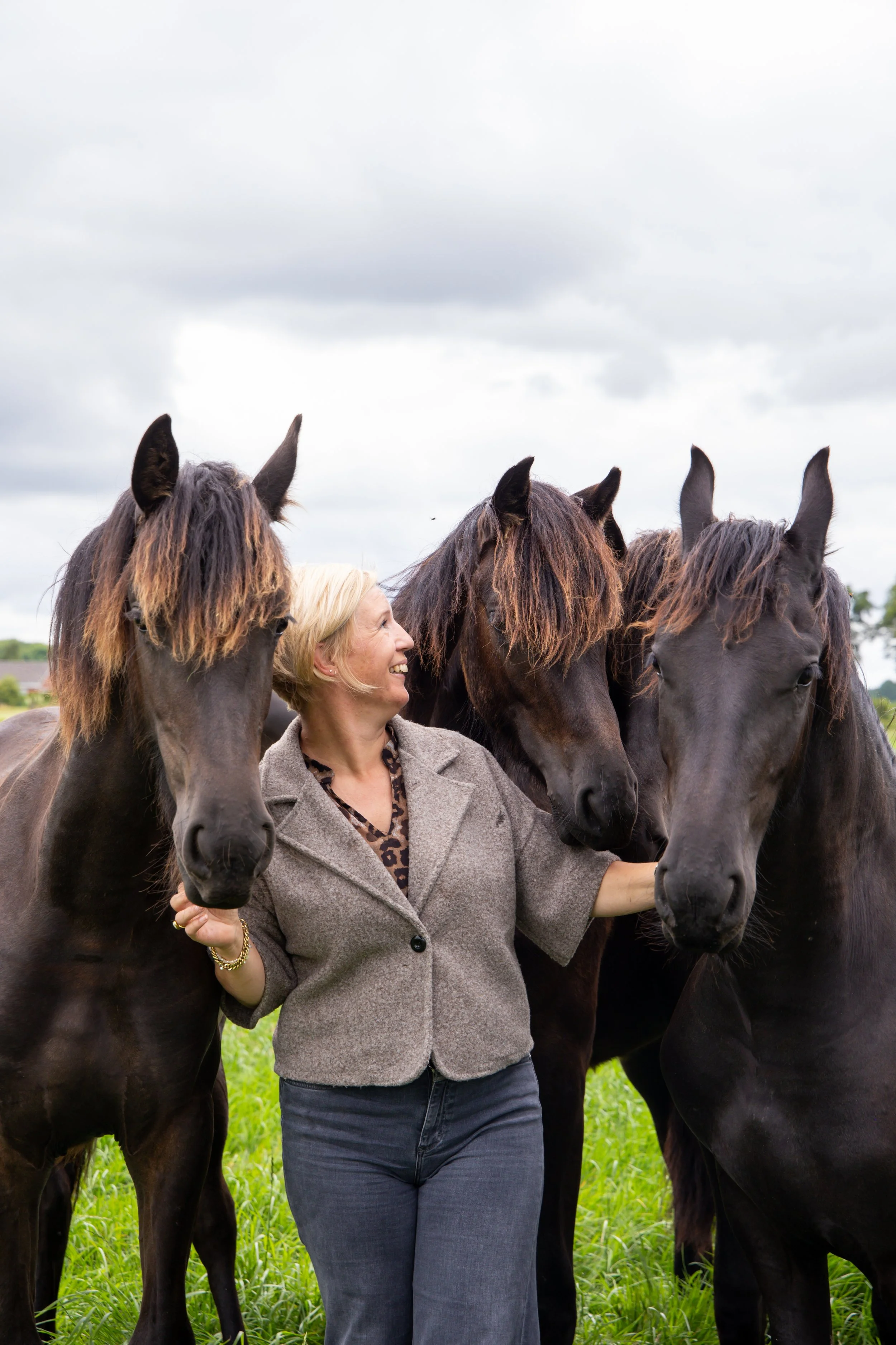 Rianne Sibma lachend tussen drie losse Friese paarden in het weiland in Rottum
