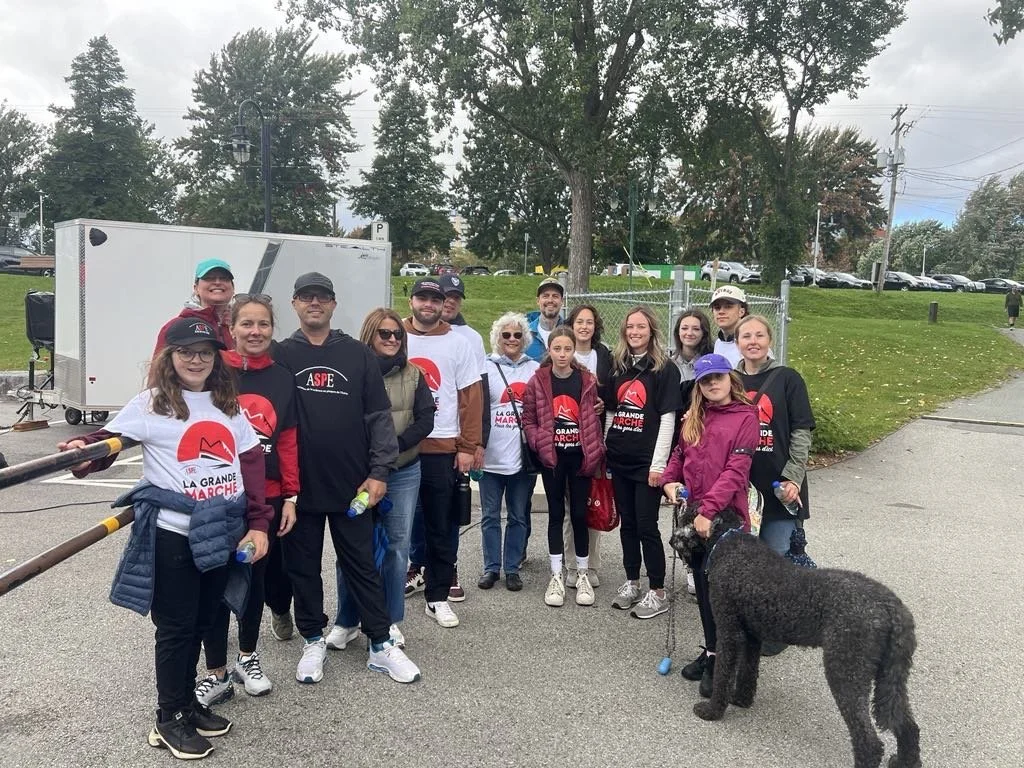 Un homme portant un sweat-shirt bleu et blanc avec un logo, debout dans un magasin de vélos rempli de divers accessoires et équipements cyclistes. Photo d'équipe pour La Grande Marche événement qui vise a supporter les gens atteints de SEP.