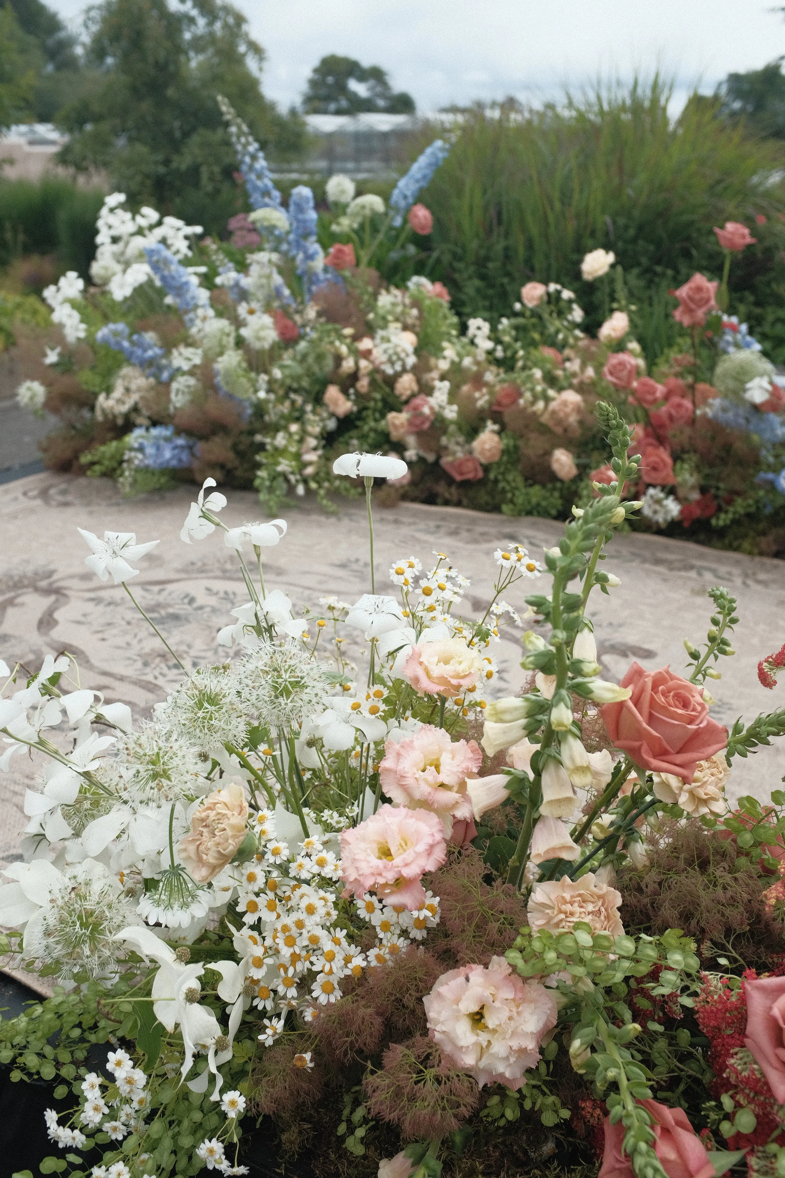 Assorted colorful flowers arranged outdoors with a background of cards and greenery.