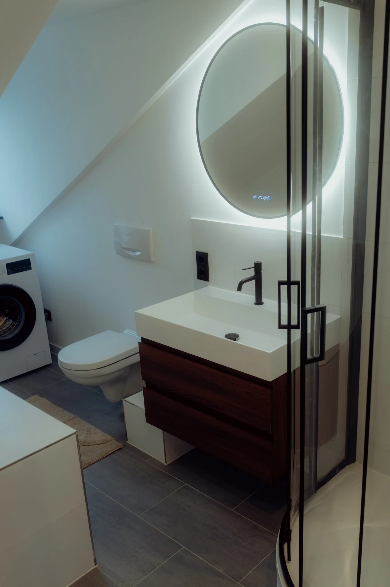 Abstract textured artwork with vertical metallic lines framed in light wood, illuminated by ceiling lights, on a white wall.