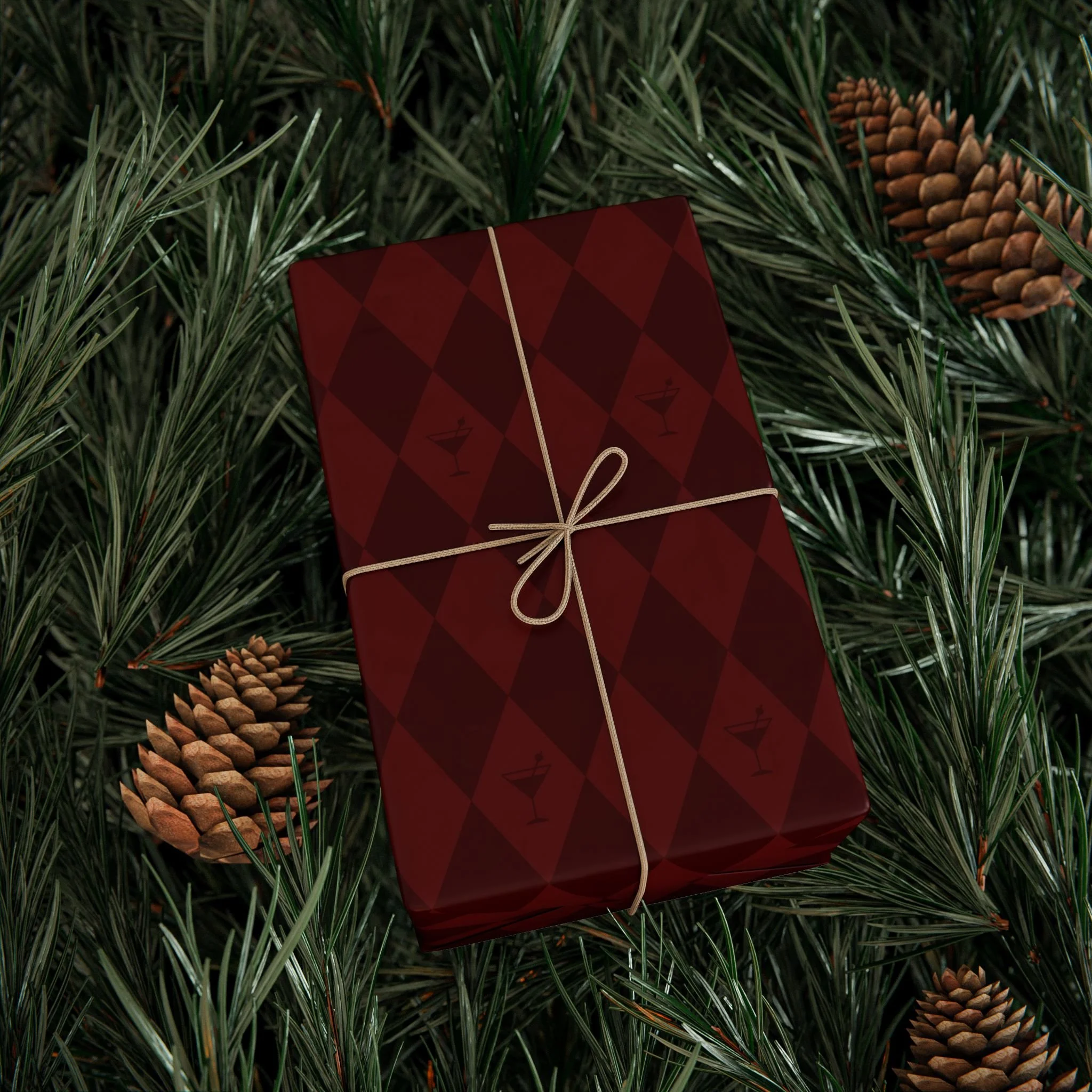 Red Christmas gift wrapped with a beige ribbon, placed on pine branches with pinecones.