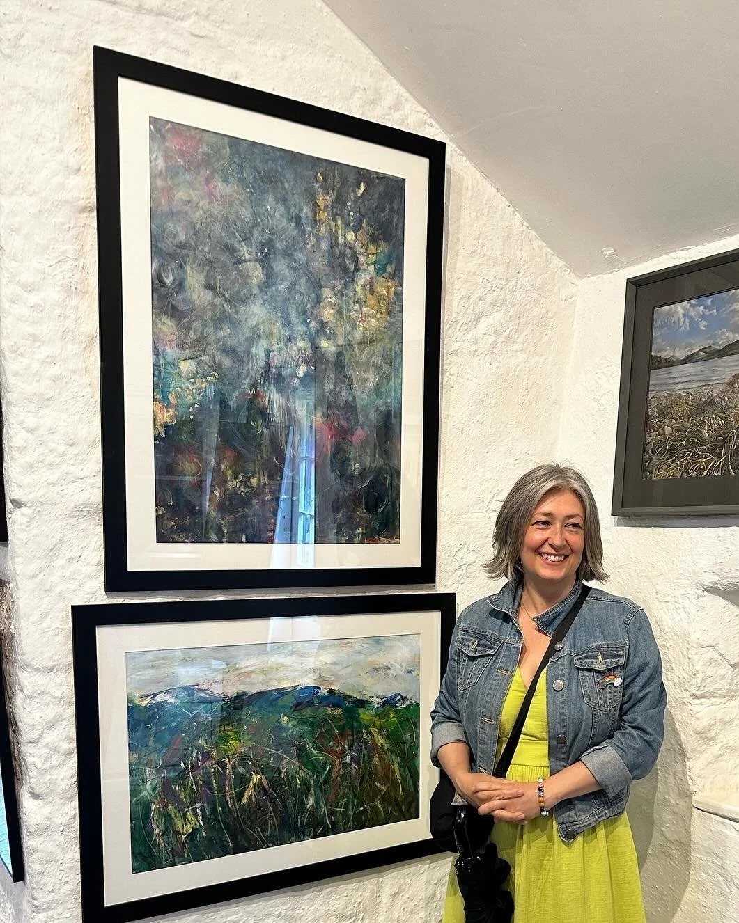Artist Catherine Burbridge standing in front of two of her original paintings on exhibit at The Old Lock Up Gallery Cromford