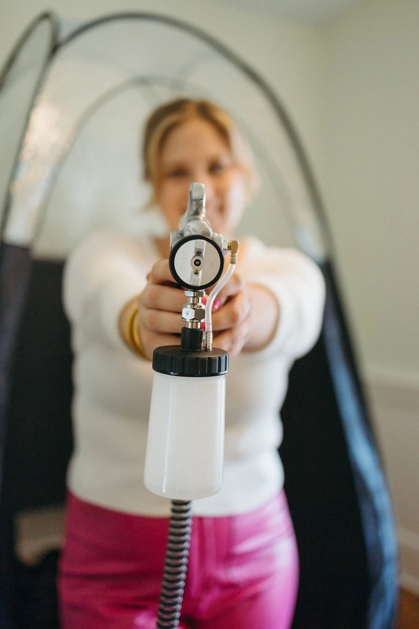 Woman pointing a gun-like device directly at the camera, with her face out of focus in the background.