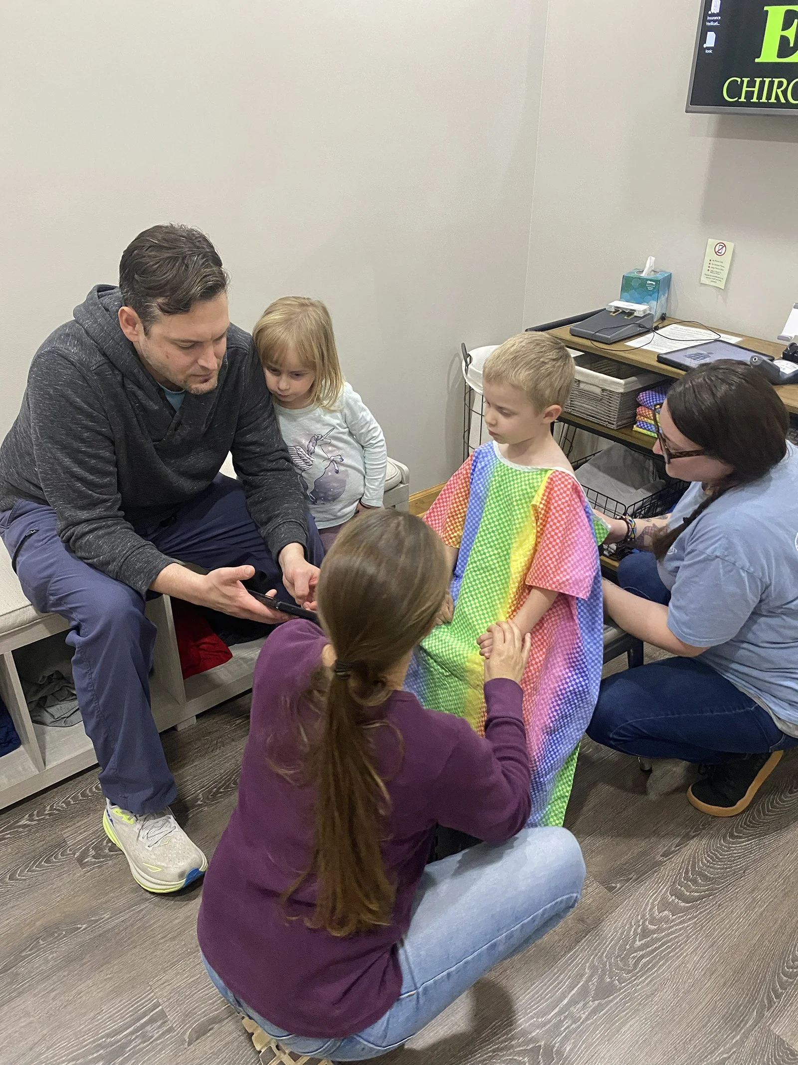 A man showing something on his phone to a group of children and a woman in a medical or clinic setting.