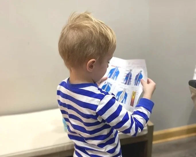 A young boy with red hair and wearing a blue and white striped shirt looking at a colorful diagram or brochure.