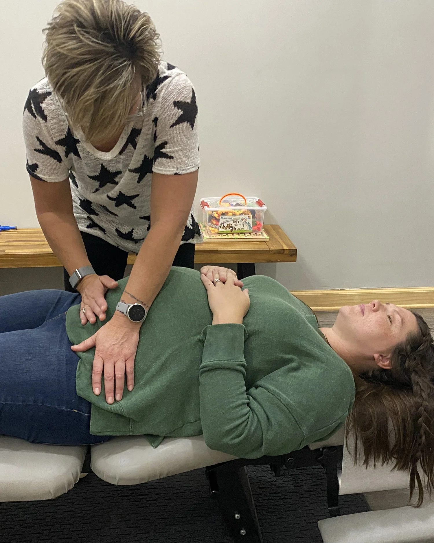 A woman performing CPR on a person lying on a treatment table in a medical setting.