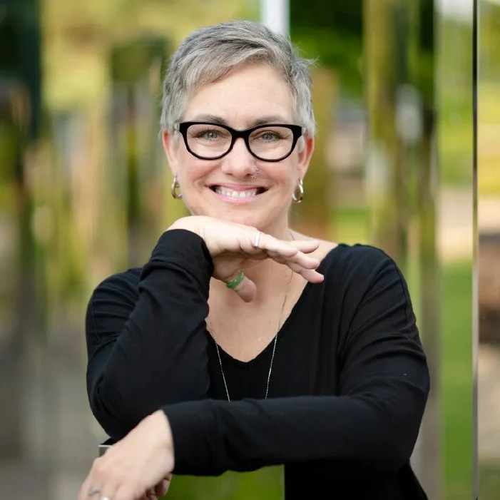 Smiling woman with short gray hair and glasses, wearing a black top, posing outdoors
