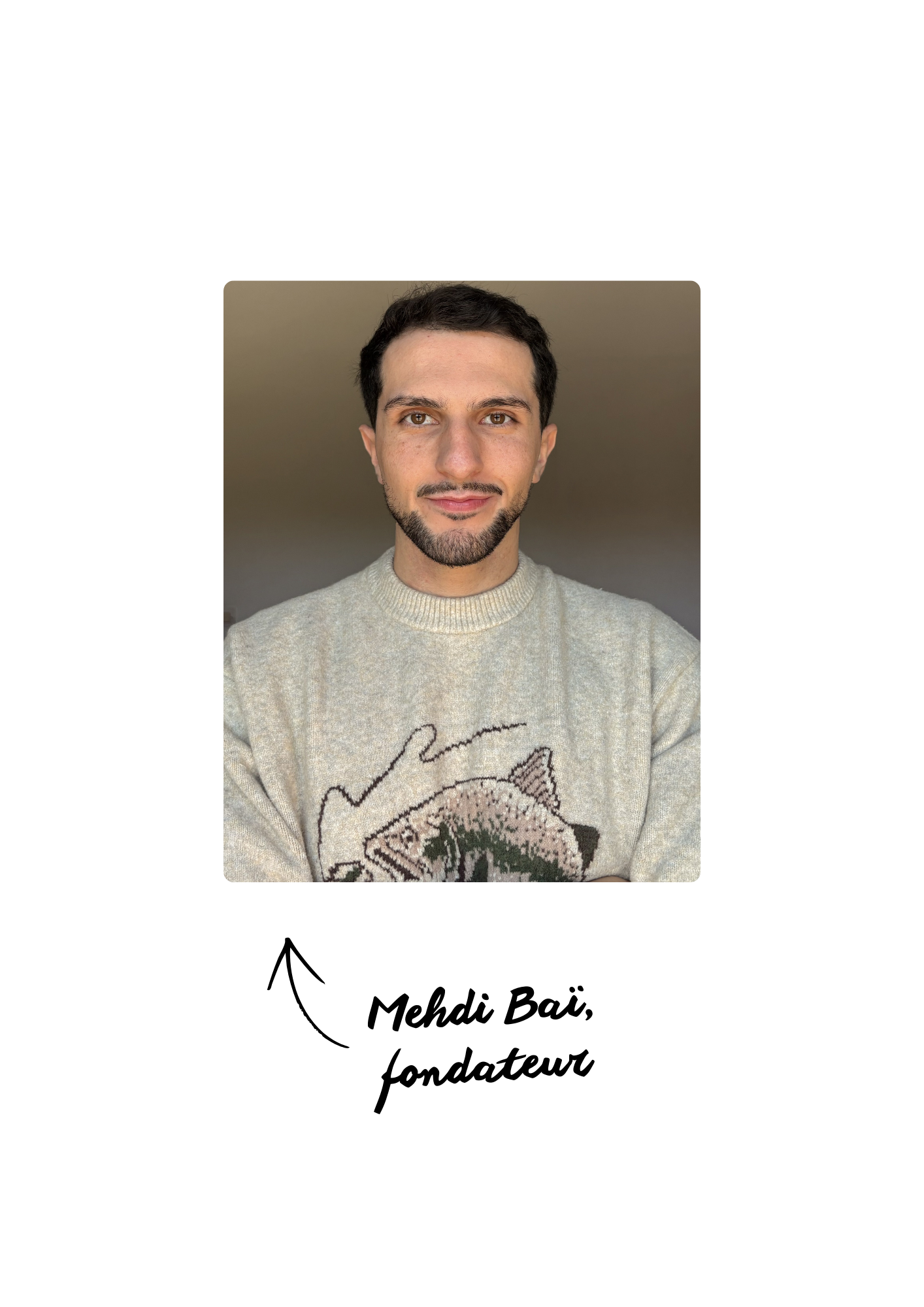 Un homme avec des cheveux courts, une barbe et portant un pull beige avec un motif de poisson, pose devant un mur neutre.