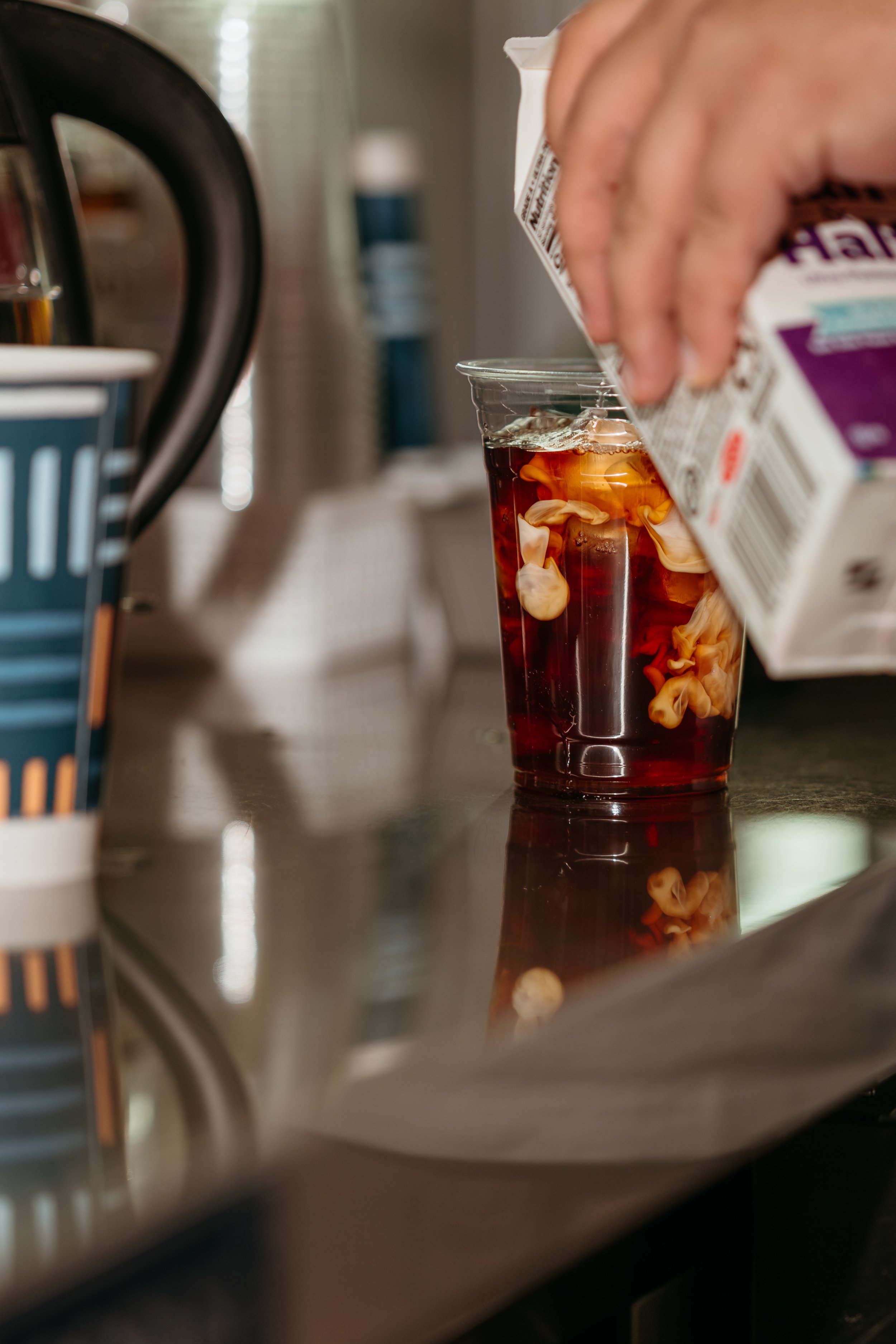 Person pouring milk into iced coffee with cream swirls.