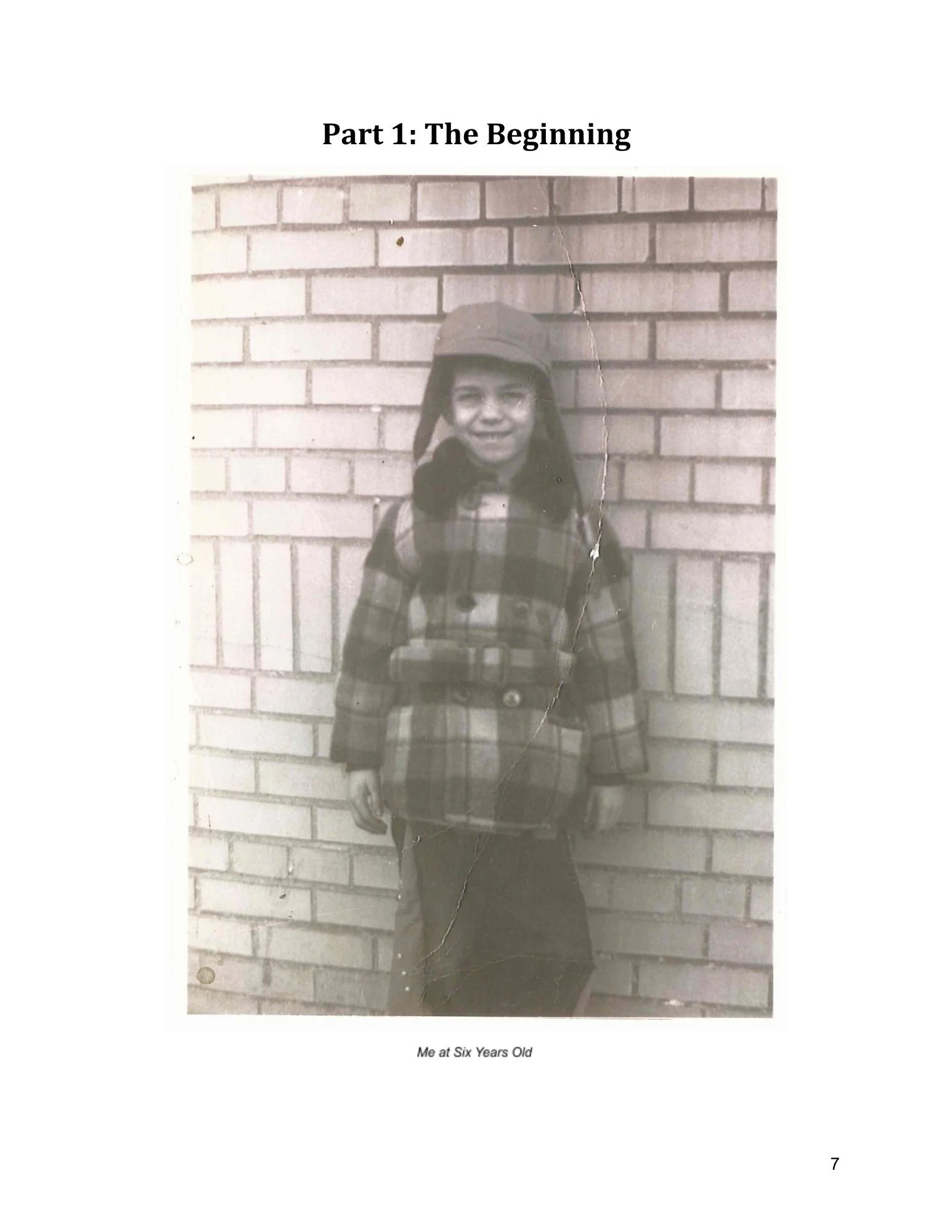Photo from a client's memoir. Black and white photograph of a young child wearing a hat, with a brick wall in the background. The photo caption reads: "Me at Six Years Old."