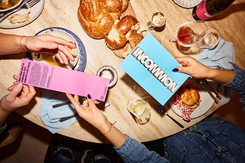 People holding colorful signs at a dinner table with bread, a burger, drinks, and utensils.