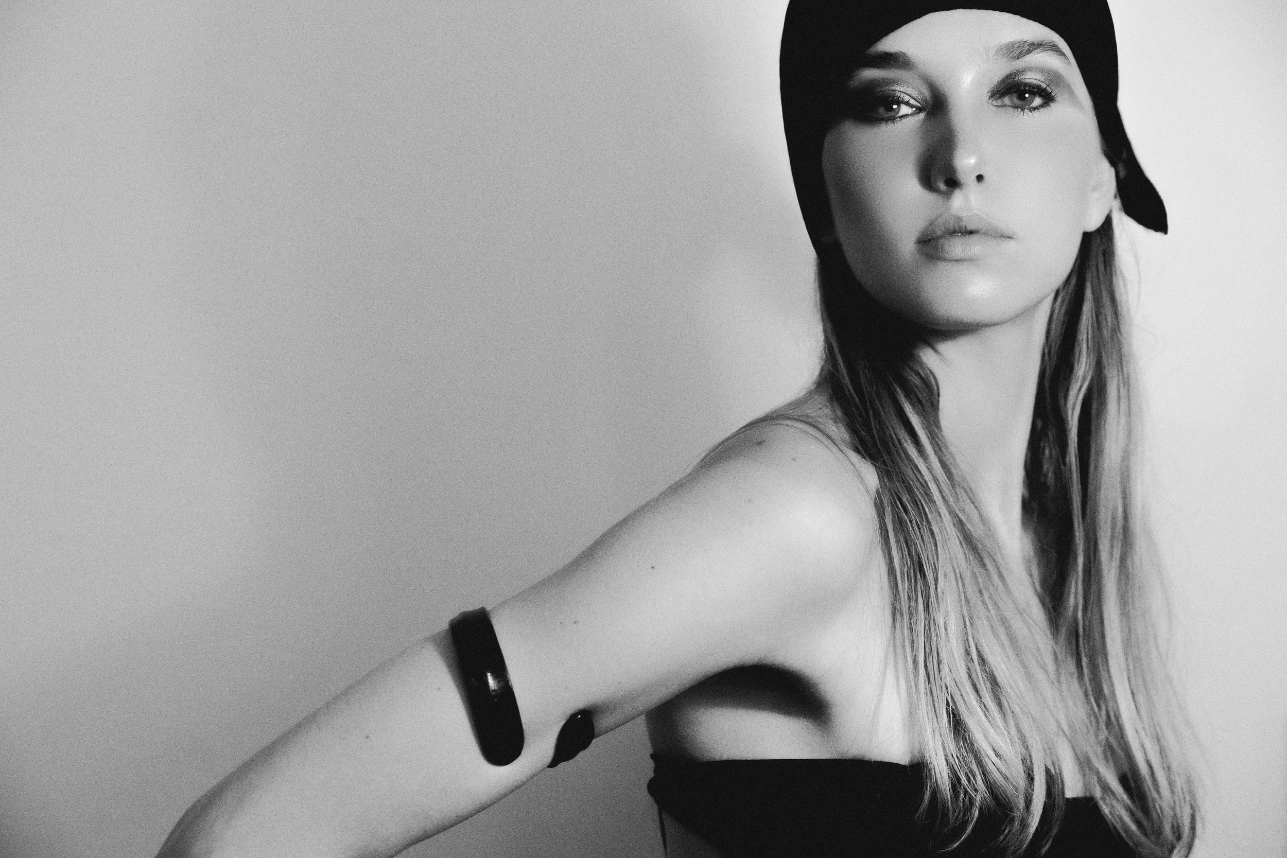 Black and white portrait of a woman with long hair, wearing a headscarf and a black strapless top, looking at the camera with a neutral expression.