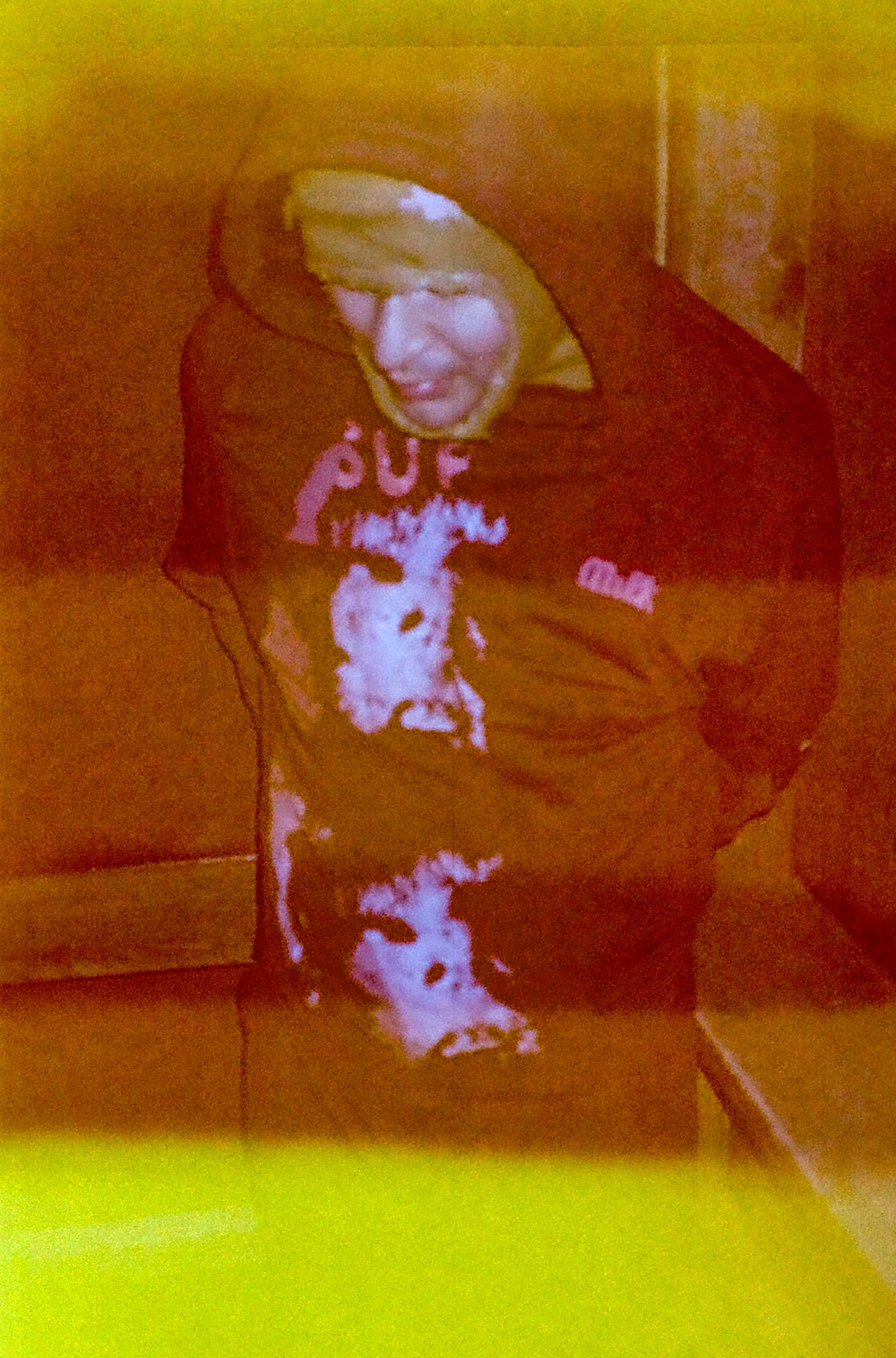 A young man wearing a black hoodie with a graphic design, standing in a corner.