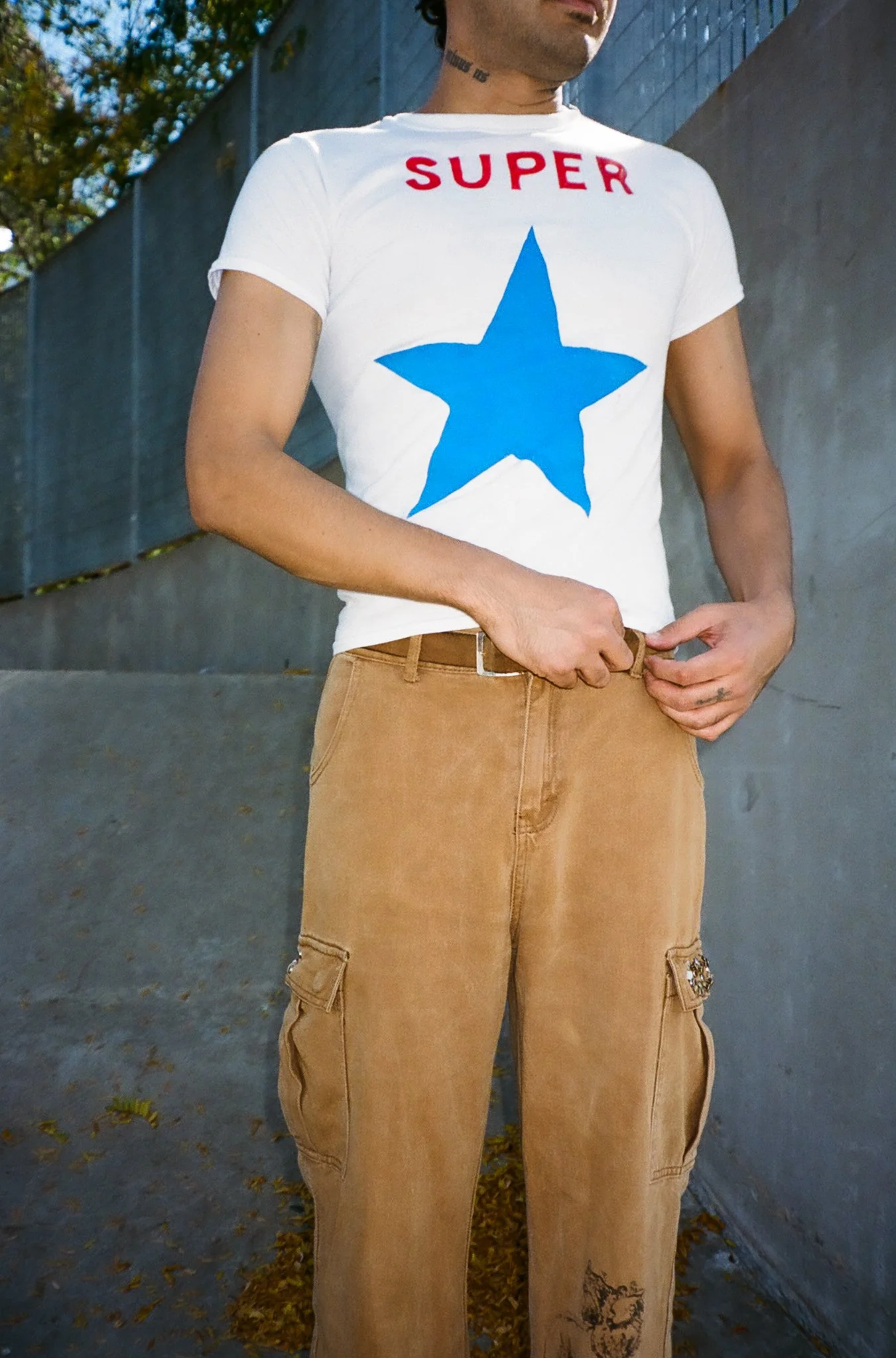 Person wearing a white t-shirt with a large blue star and red text that says 'SUPER' on the front, standing outdoors.