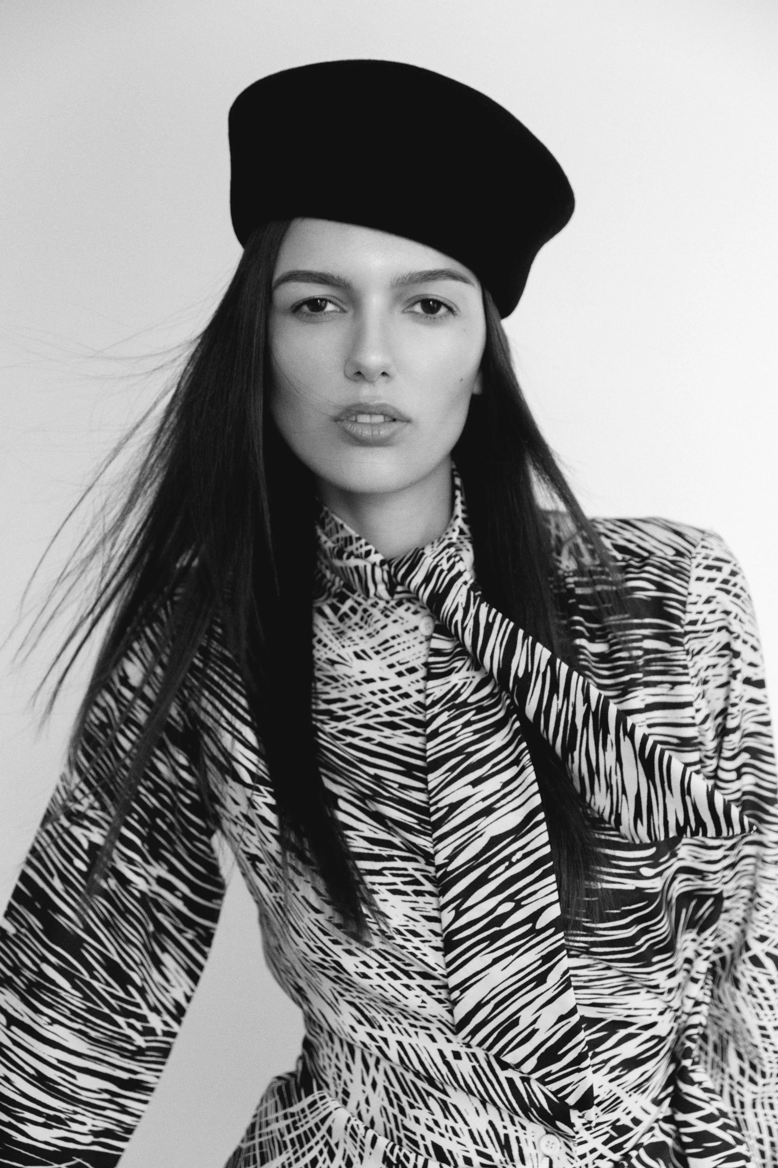 Black and white photo of a woman wearing a hat and patterned shirt.