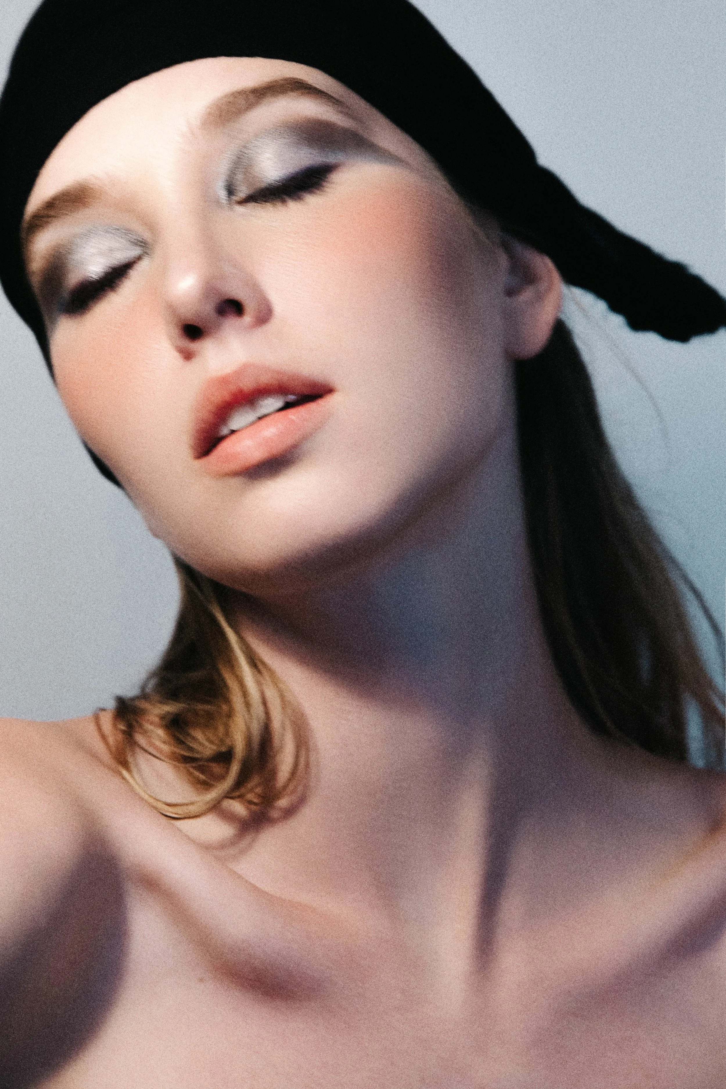 Close-up of a woman with silver eye makeup, wearing a black headscarf, with lips slightly parted and a soft expression.