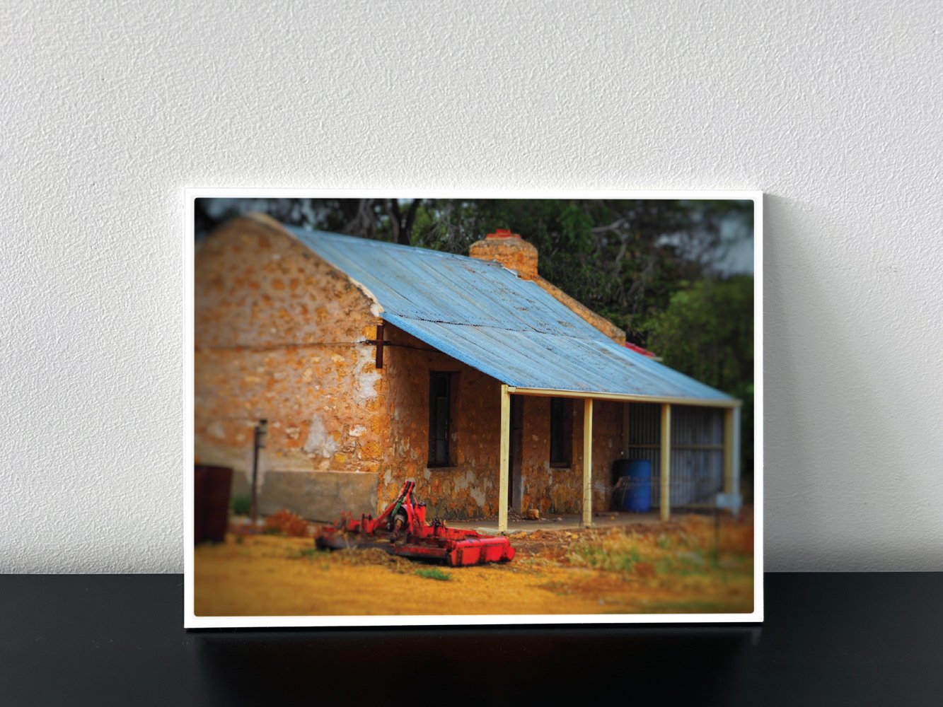 Metal backed photo of an old stone house with a blue metal roof in Australian countryside.