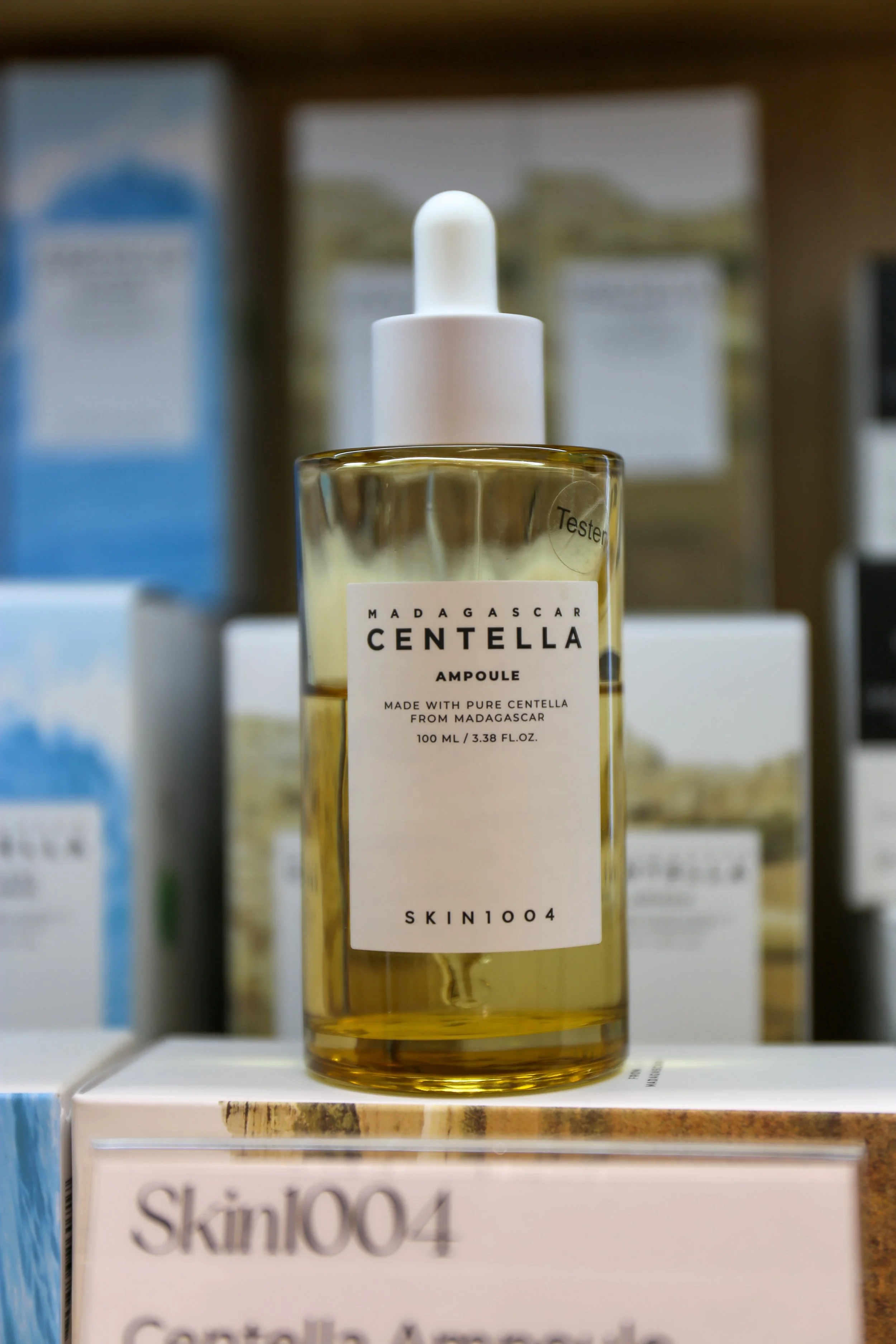 A bottle of Madagascar Centella Ampoule with a white dropper cap, sitting on a retail display shelf amidst other skincare boxes.