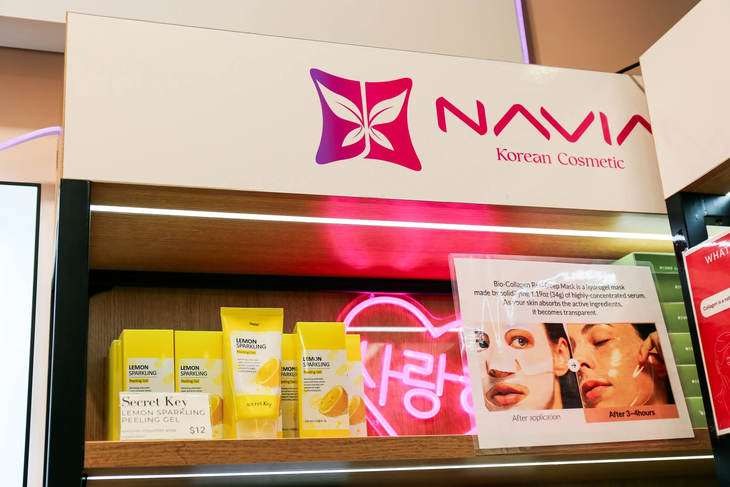 Display shelf with yellow boxes of Secret Key Lemon Sparkling Peeling Gel, a poster showing the effects of a bio-collagen mask, and a sign for NAVIA Korean Cosmetic.