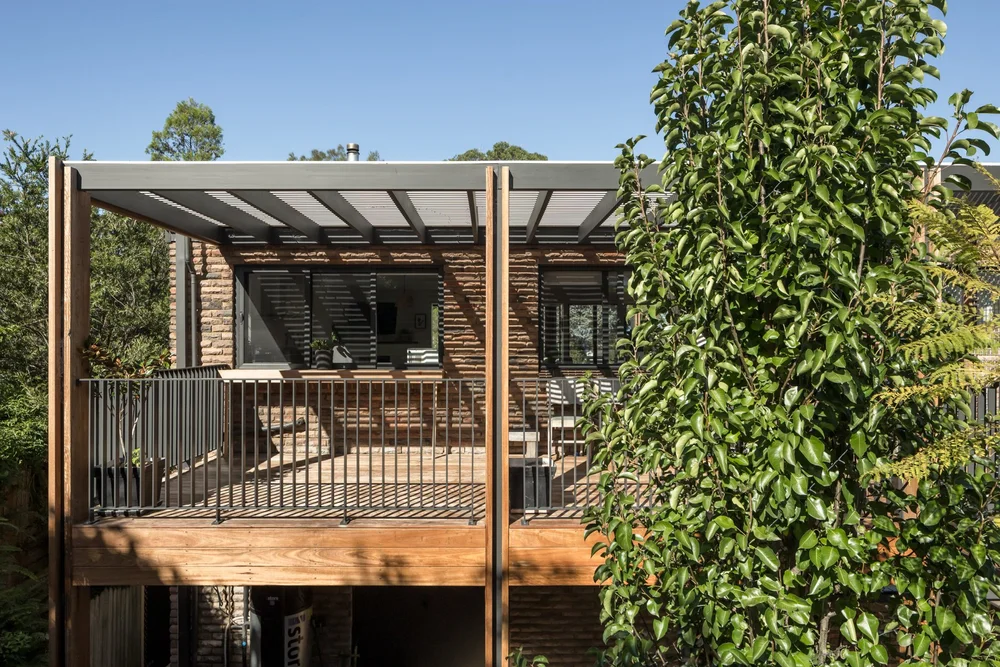 Timber-framed rear deck with black balustrade and brick lower level among trees at Elanora Four, Coledale, by CKS Projects