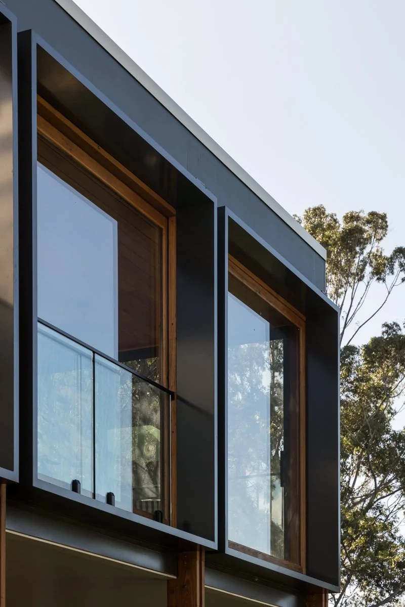 Close-up of dark window frames set into timber reveals with a glass balustrade, Coledale project detail by CKS Projects
