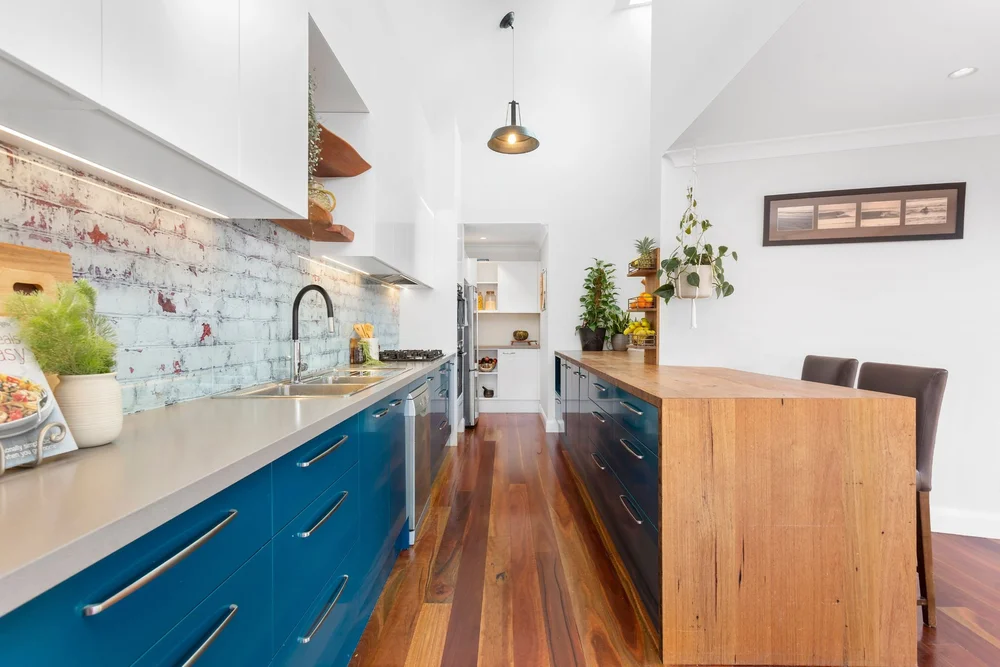 Kitchen in The Barn Woonona with blue cabinetry, a timber island bench and a brick feature wall, built by CKS Projects