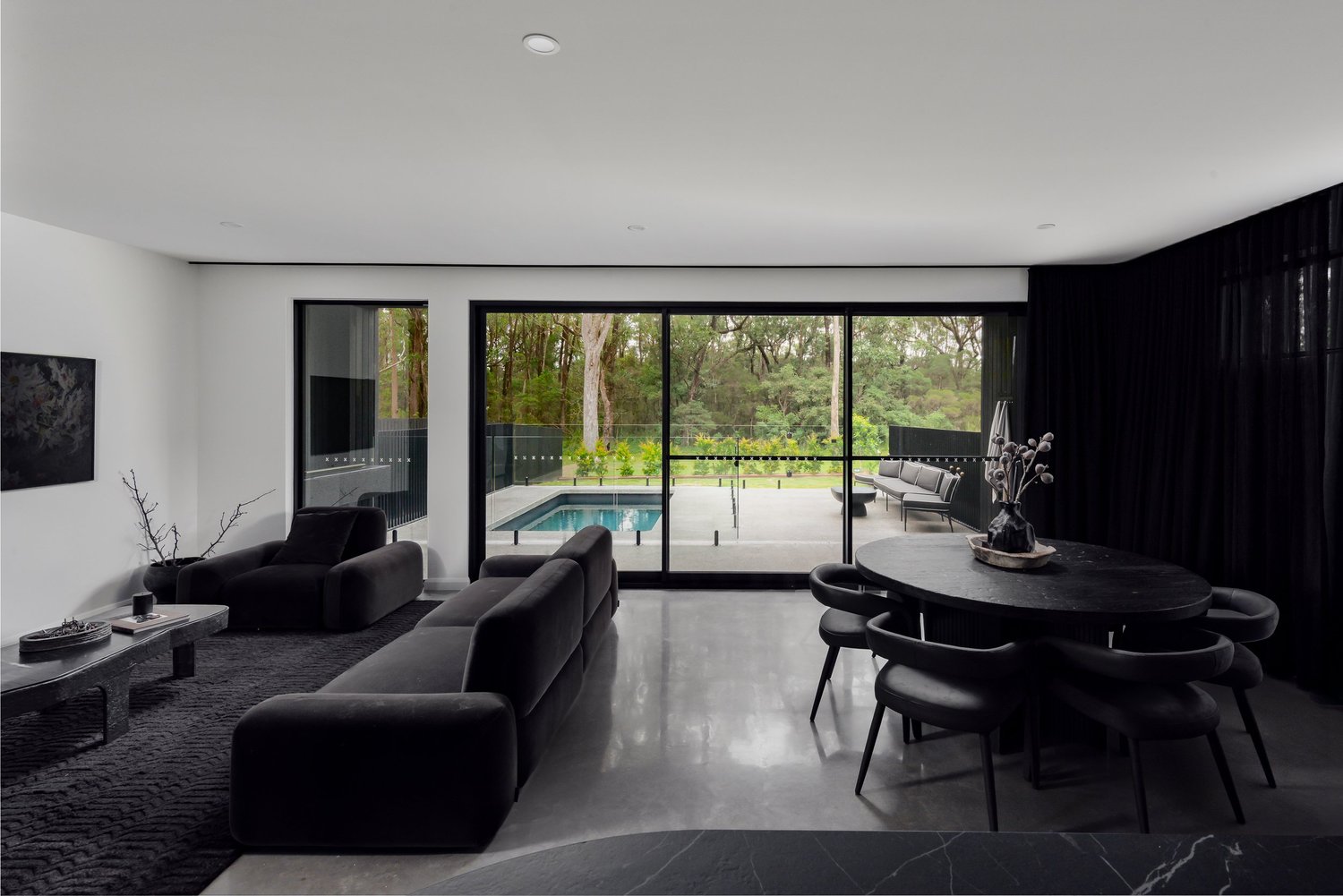 Open-plan living and dining with black furniture and polished concrete floors, opening to the pool at the Huskisson Duplex