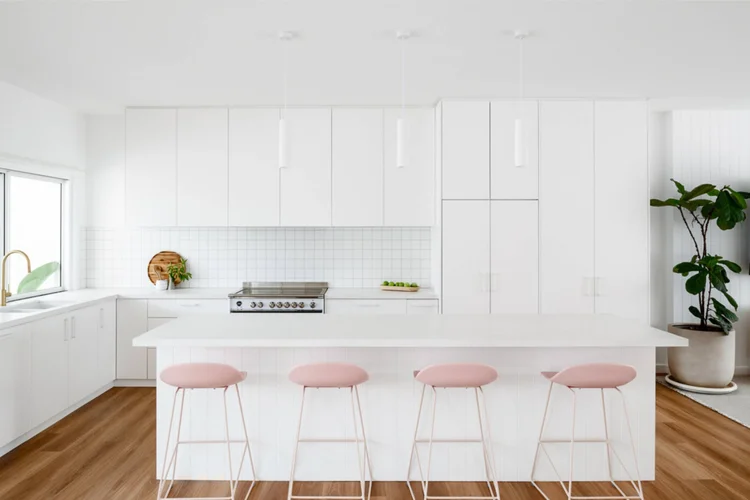 White kitchen with a long island bench and pink stools on oak flooring at the Warilla Beach House