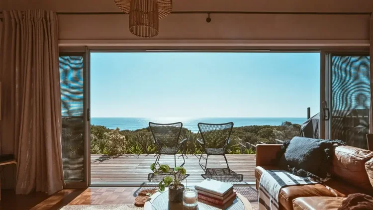 Living room opening through wide doors to a timber deck and ocean view